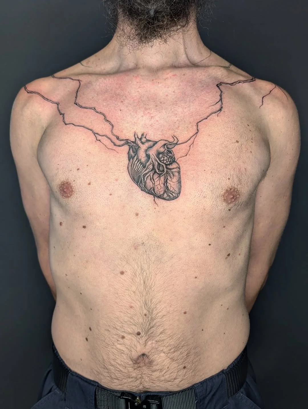 Tattoo of a human heart with lightning bolts extending from it on a man's chest.