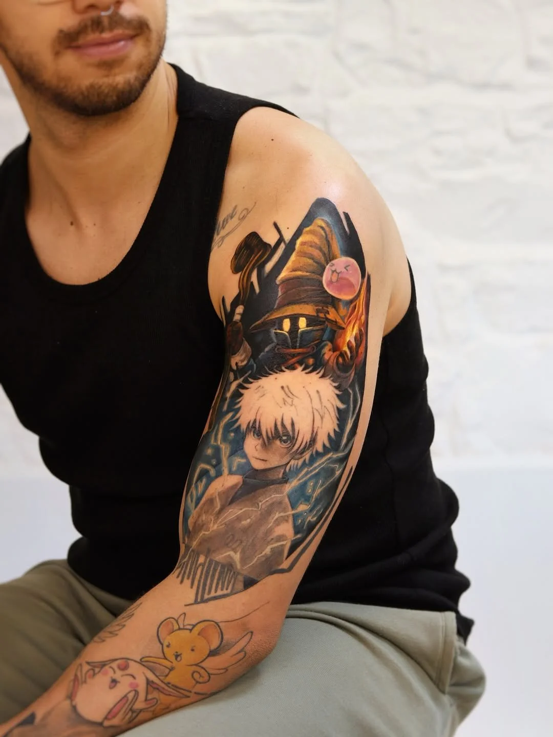Tattoo of a young anime character with white hair surrounded by blue lightning on a person's upper arm, with cartoonish characters near the wrist.