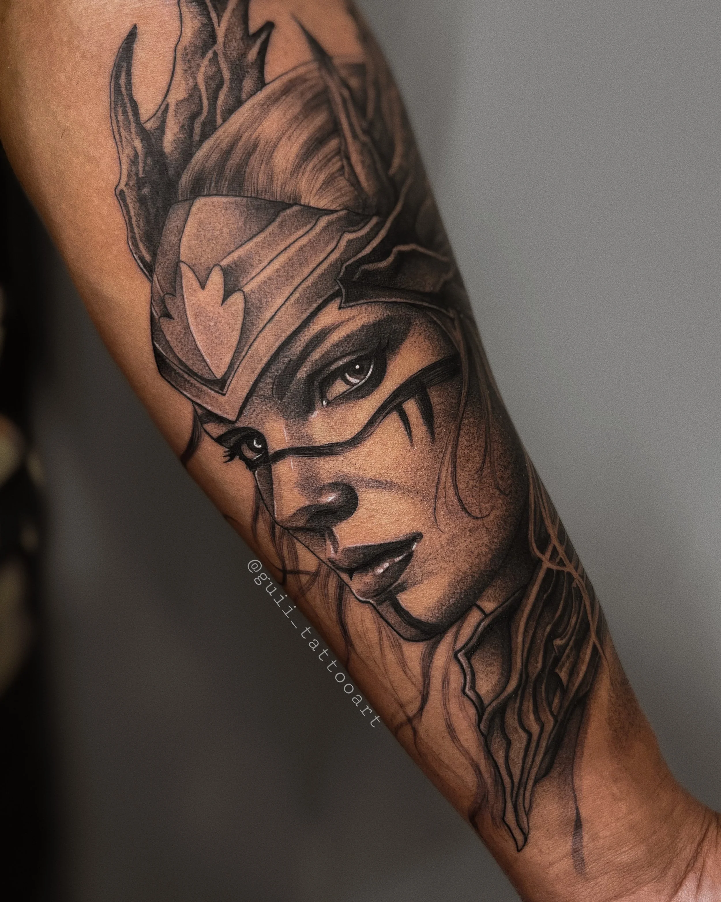 Detailed tattoo of a warrior woman with a helmet on an arm, featuring intricate shading and a strong gaze.