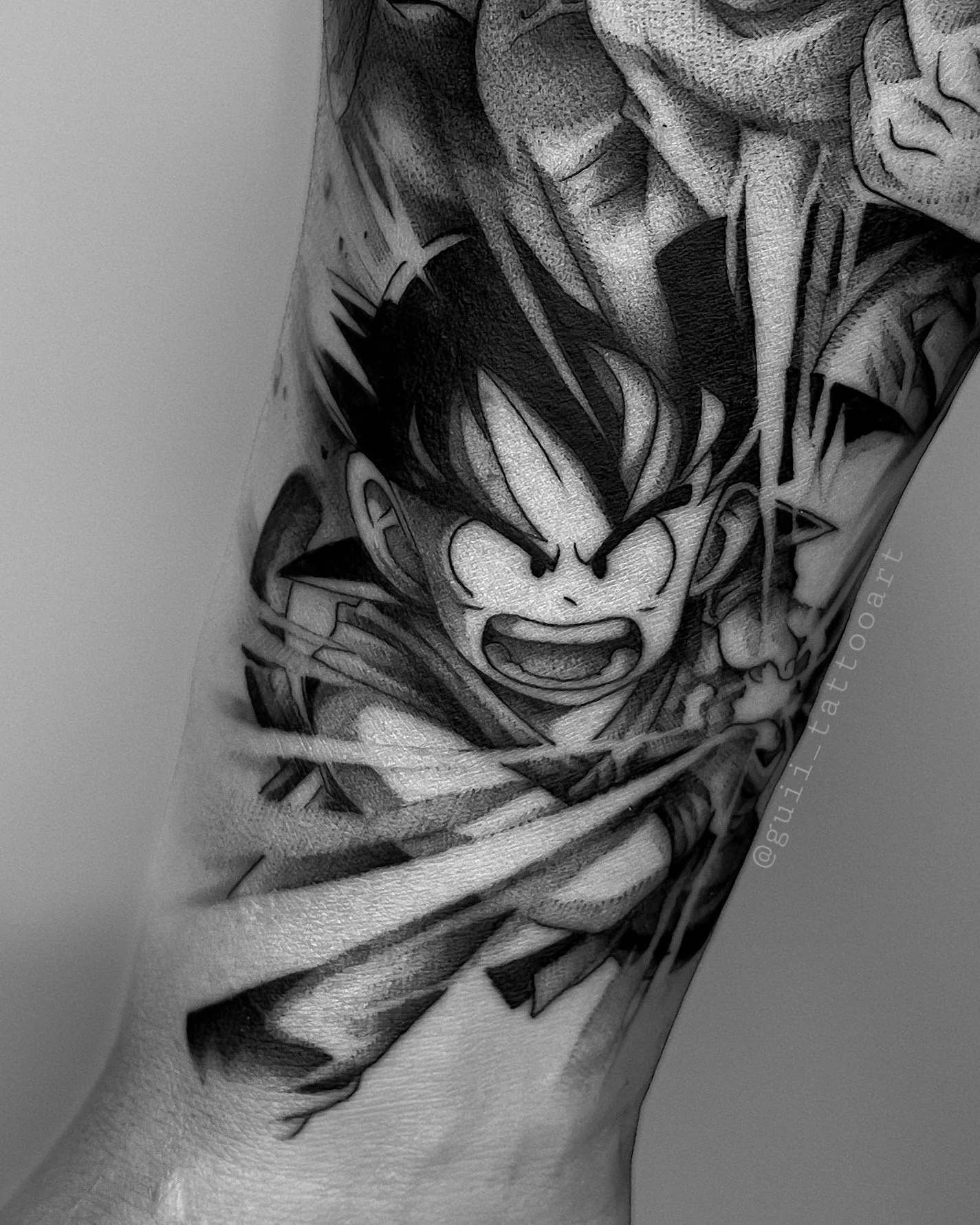 Black and gray tattoo of an animated character with spiky hair, shouting, surrounded by dynamic lines and shading on forearm.