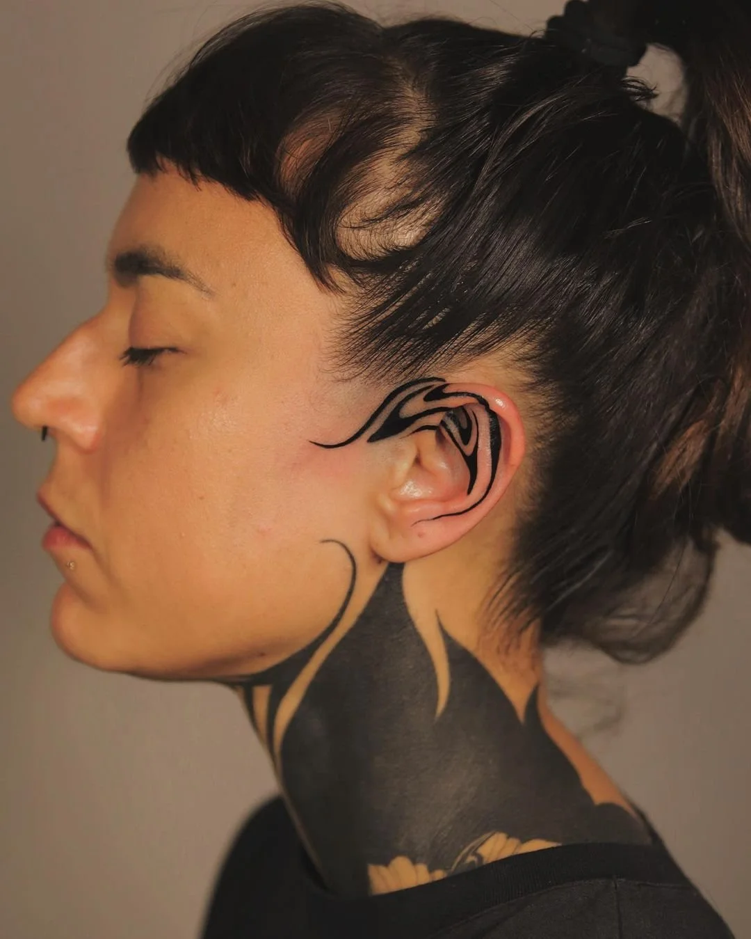 Person with intricate black tattoos on ear and neck, side profile view.