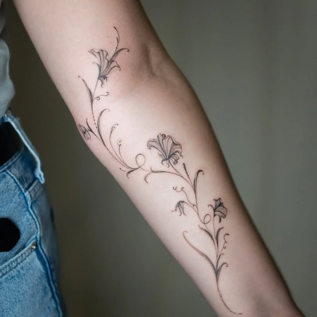 Delicate black floral tattoo on person's forearm with intricate swirls and leaf details.