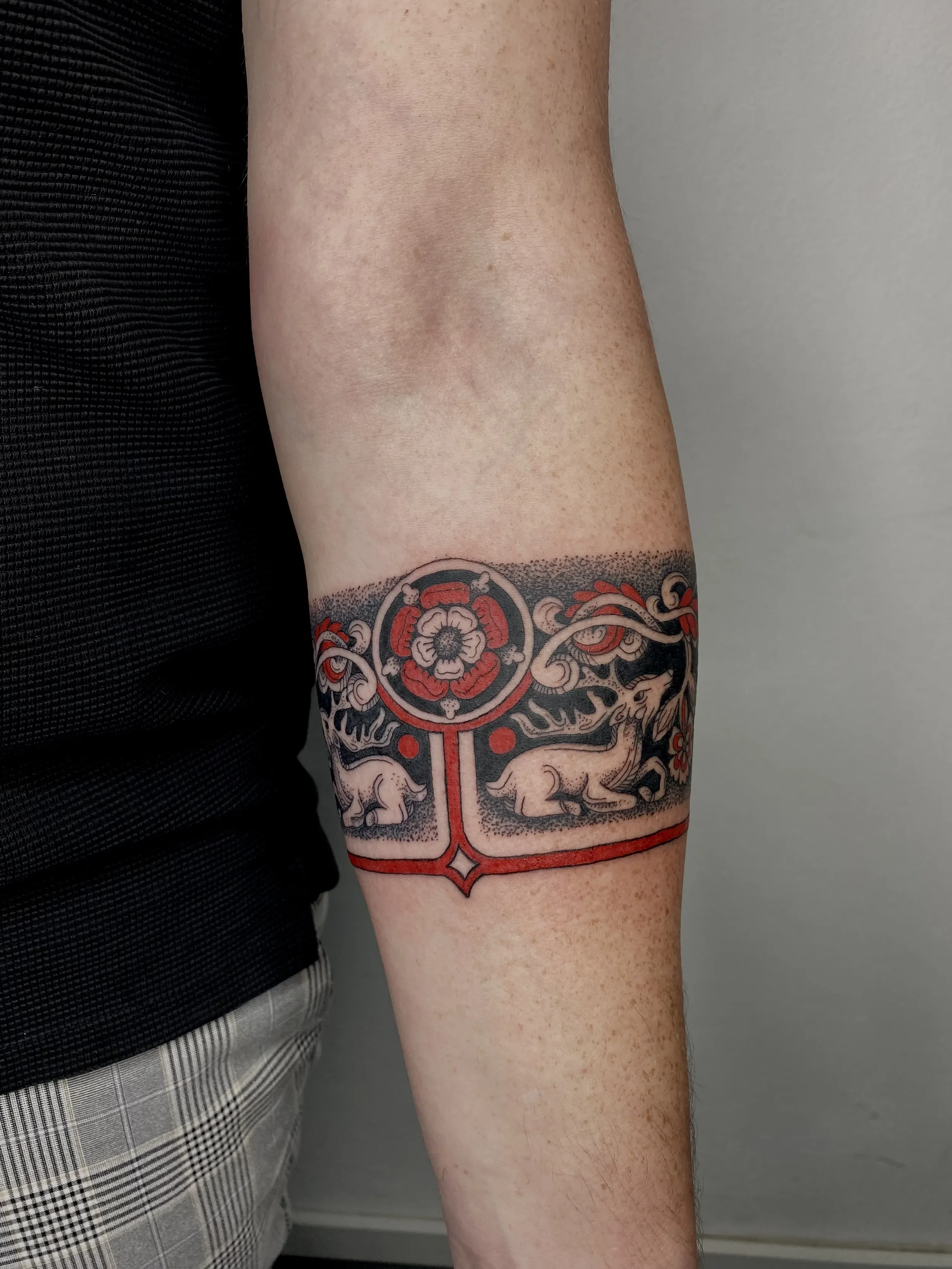 A tattoo on a person's forearm featuring two mice facing each other, surrounded by decorative floral and geometric elements in black, red, and gray ink.