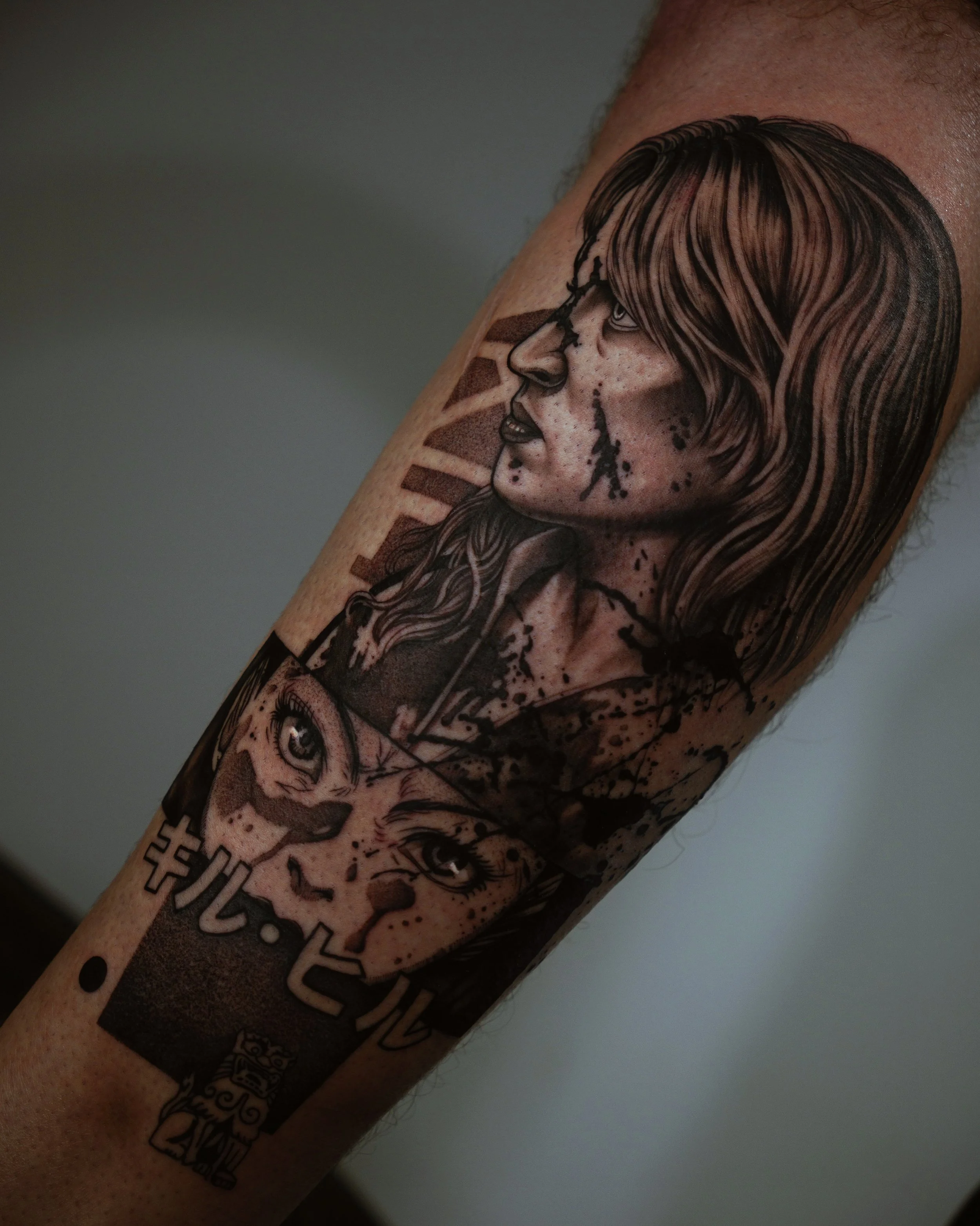 Black and gray tattoo featuring a detailed portrait of a woman with long hair, Japanese text, and ink splatters, on a person's arm.