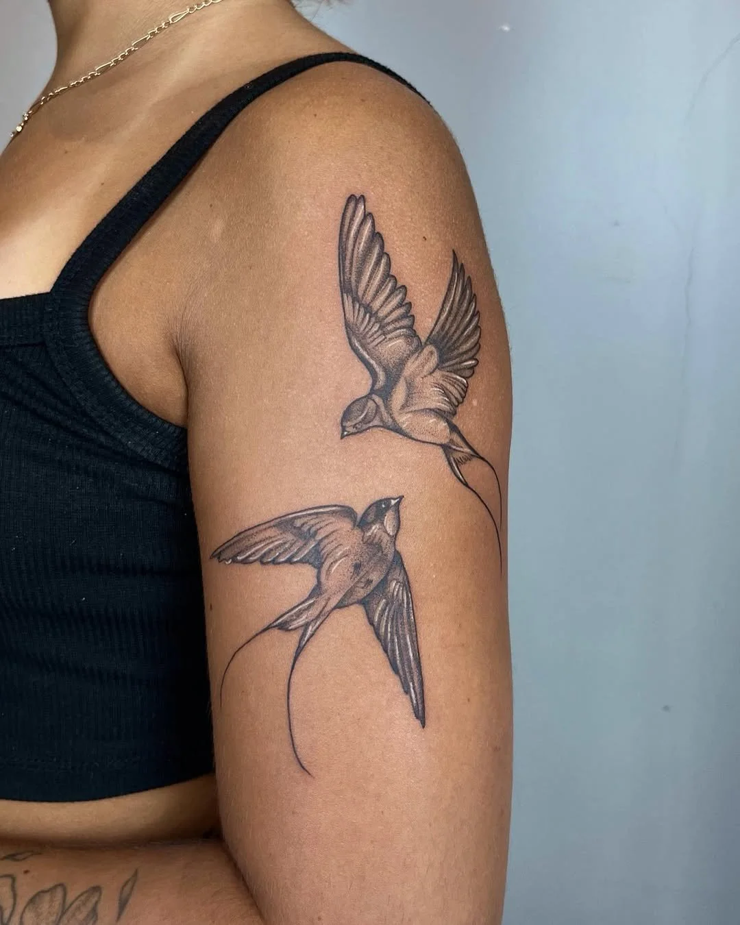 Tattoo of two flying birds on a person's upper arm, one above the other, with detailed wings and tails.