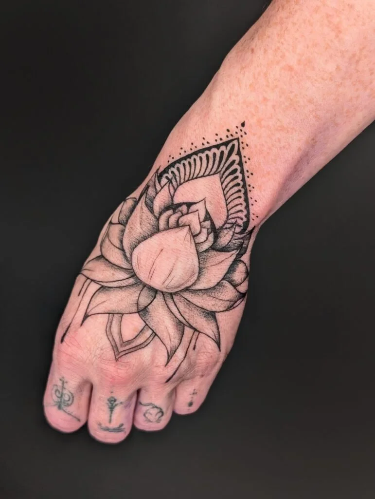 Black outlined floral tattoo on the top of a person's foot, with small symbols tattooed on toes.