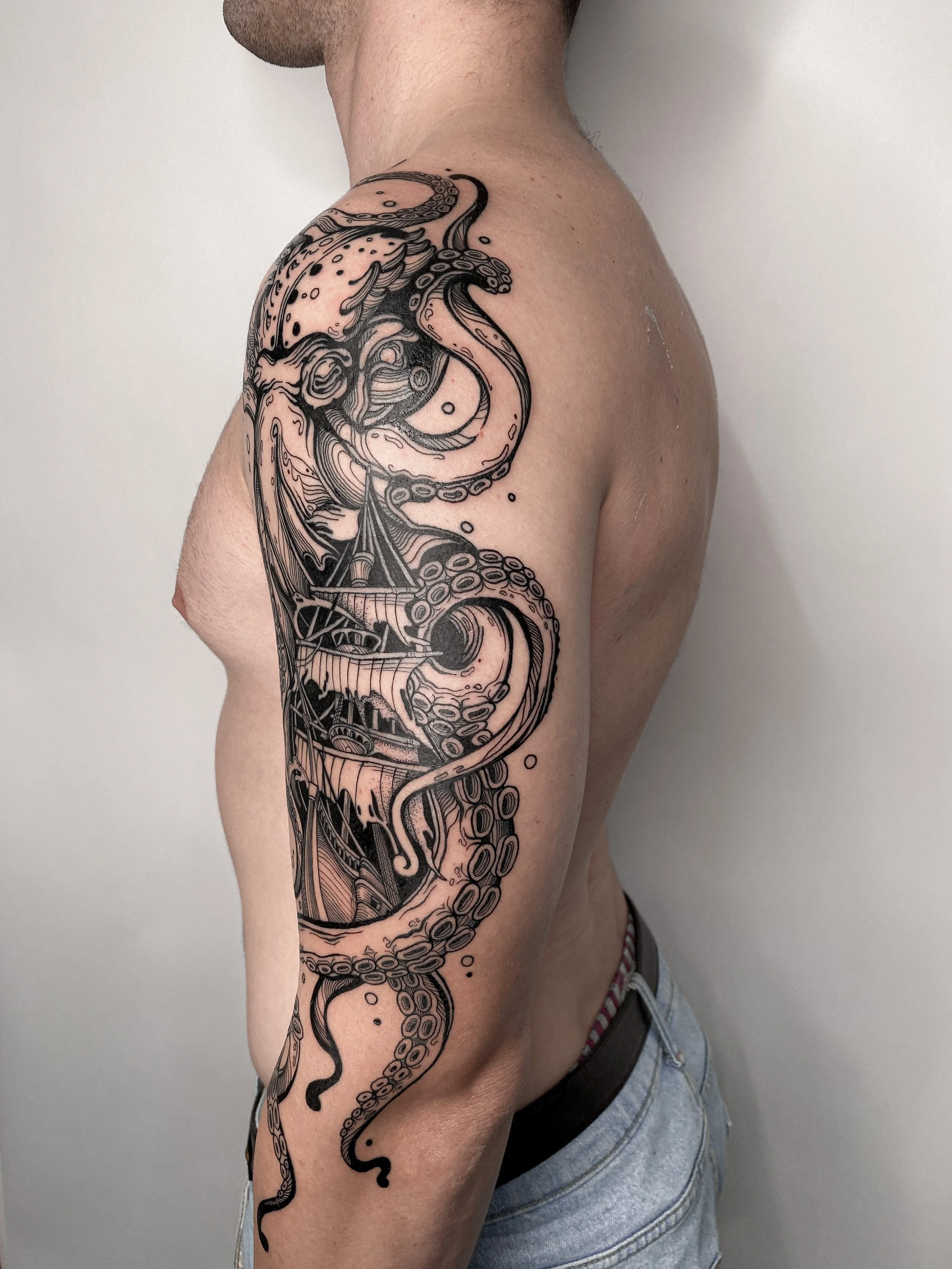 Black and gray tattoo of an octopus wrapped around a ship located on the person's upper arm and shoulder.