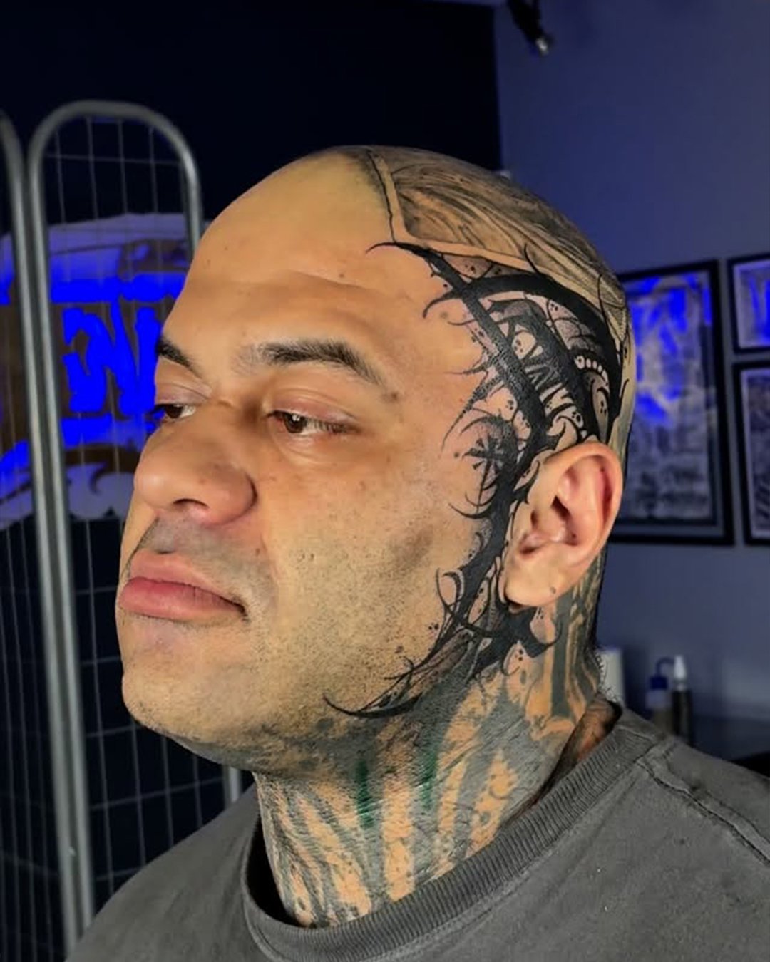 Man with tattoos on face, neck, and head, looking to the left, with tattooed scalp and large face tattoo.