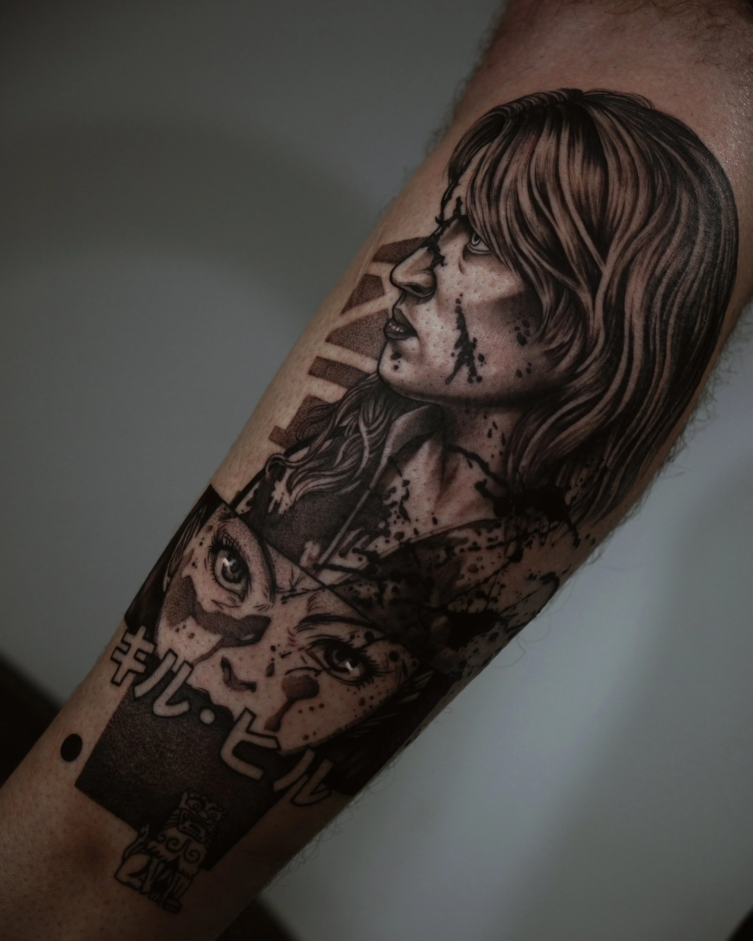 Tattoo of two serious-looking faces with long hair and Japanese text, featuring artistic shading and ink splatters on skin.