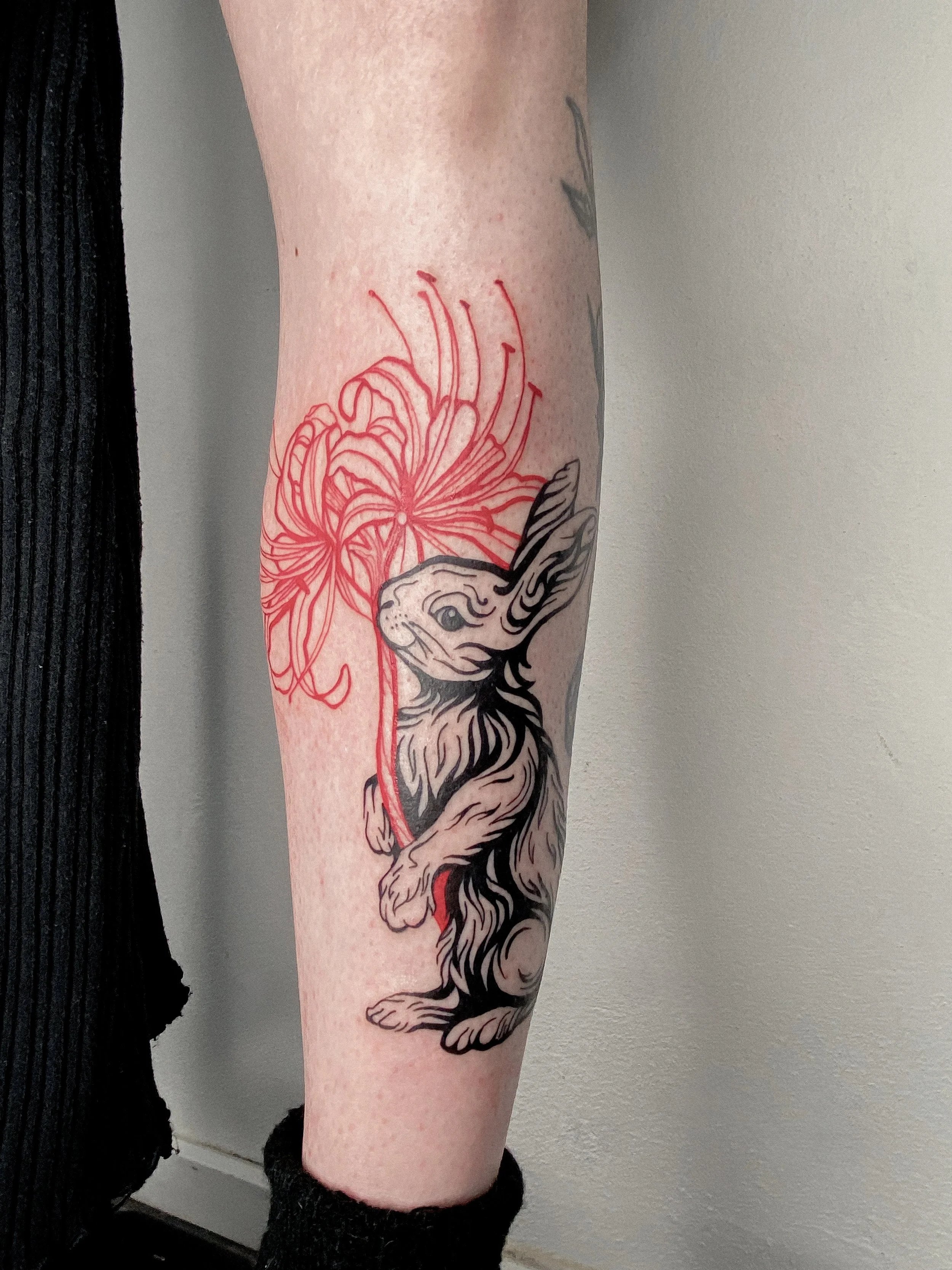 Tattoo of a bunny with a large red flower in front of its face on a person's forearm.