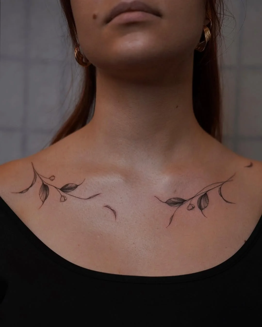 A woman with tattoos of delicate branches and leaves on her collarbone area.