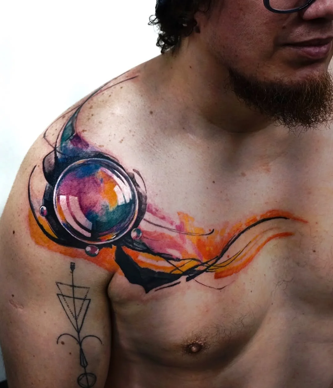 Abstract watercolor tattoo on man's shoulder and chest, featuring geometric and swirl designs in vibrant colors.