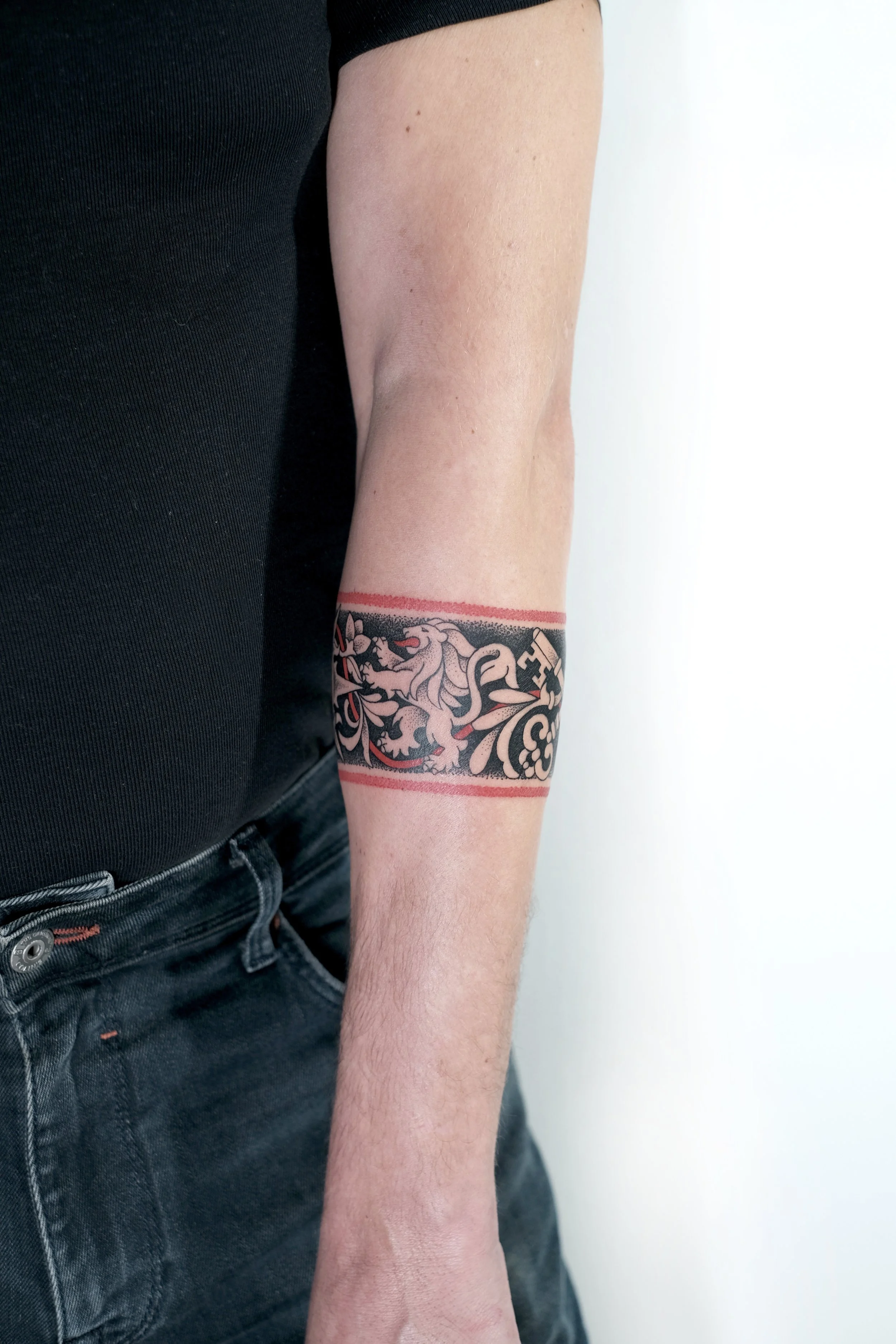 A person's arm with a tattoo of a lion and floral design surrounded by two red lines on the forearm.