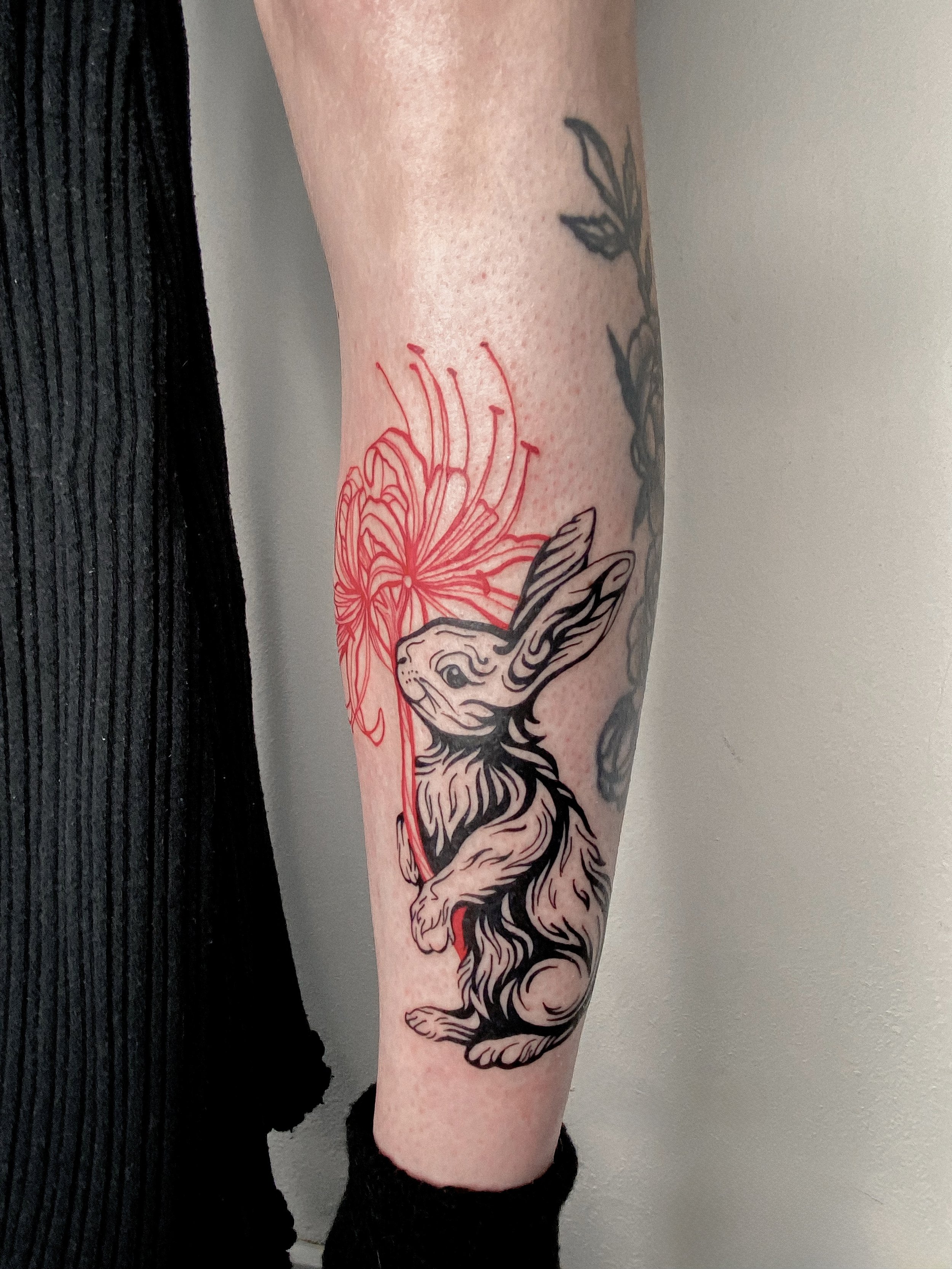 Tattoo of a hare with a red flower and lines on the person's arm.