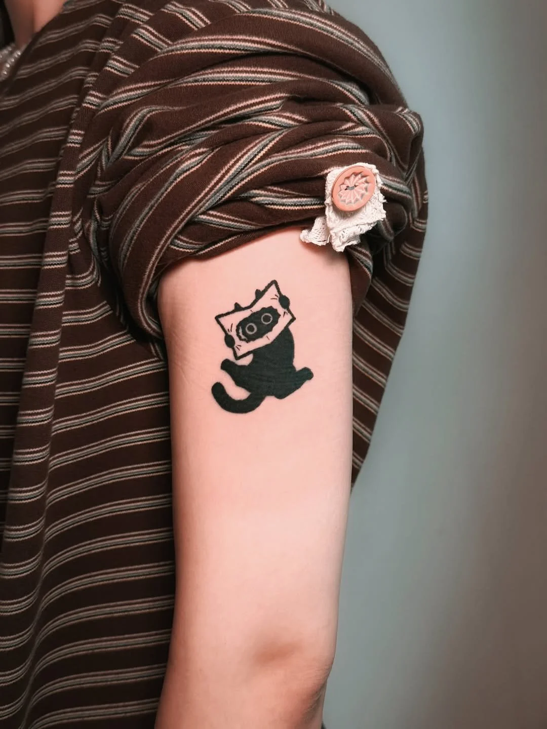 Tattoo of a black cat with a cassette tape over its face on a person's upper arm, with the person's sleeve rolled up.