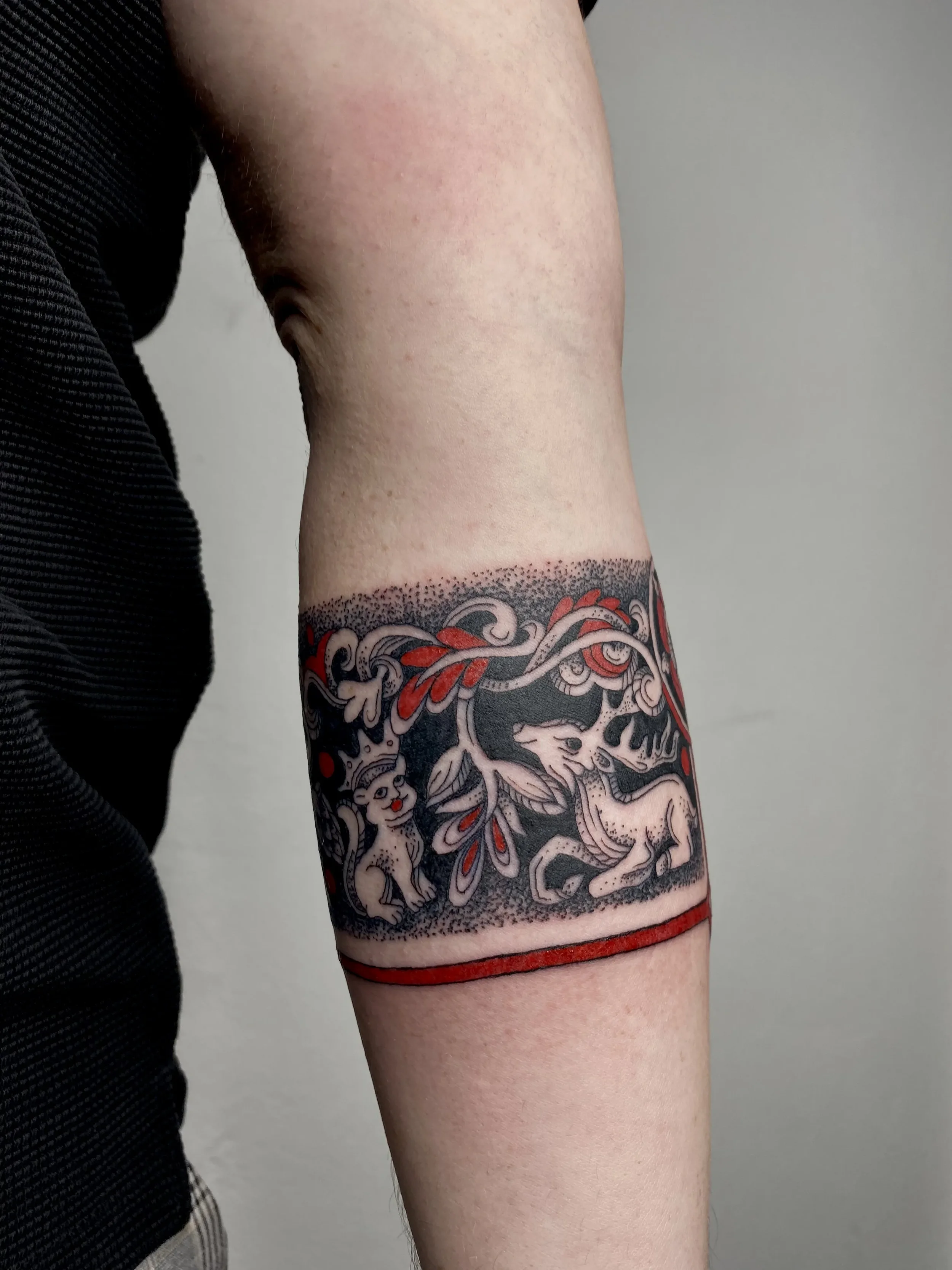 Tattoo of a wolf and a smaller animal, possibly a fox or dog, surrounded by decorative elements on a person's arm.