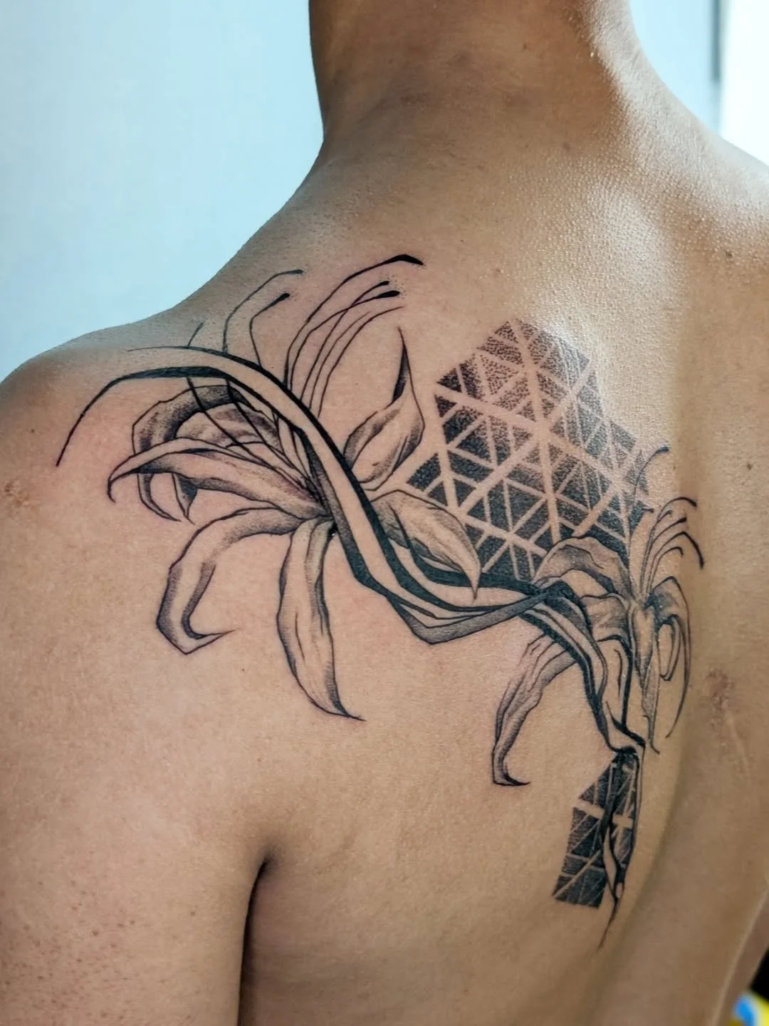 A tattoo of a lily flower and geometric patterns on a person's shoulder and upper chest.