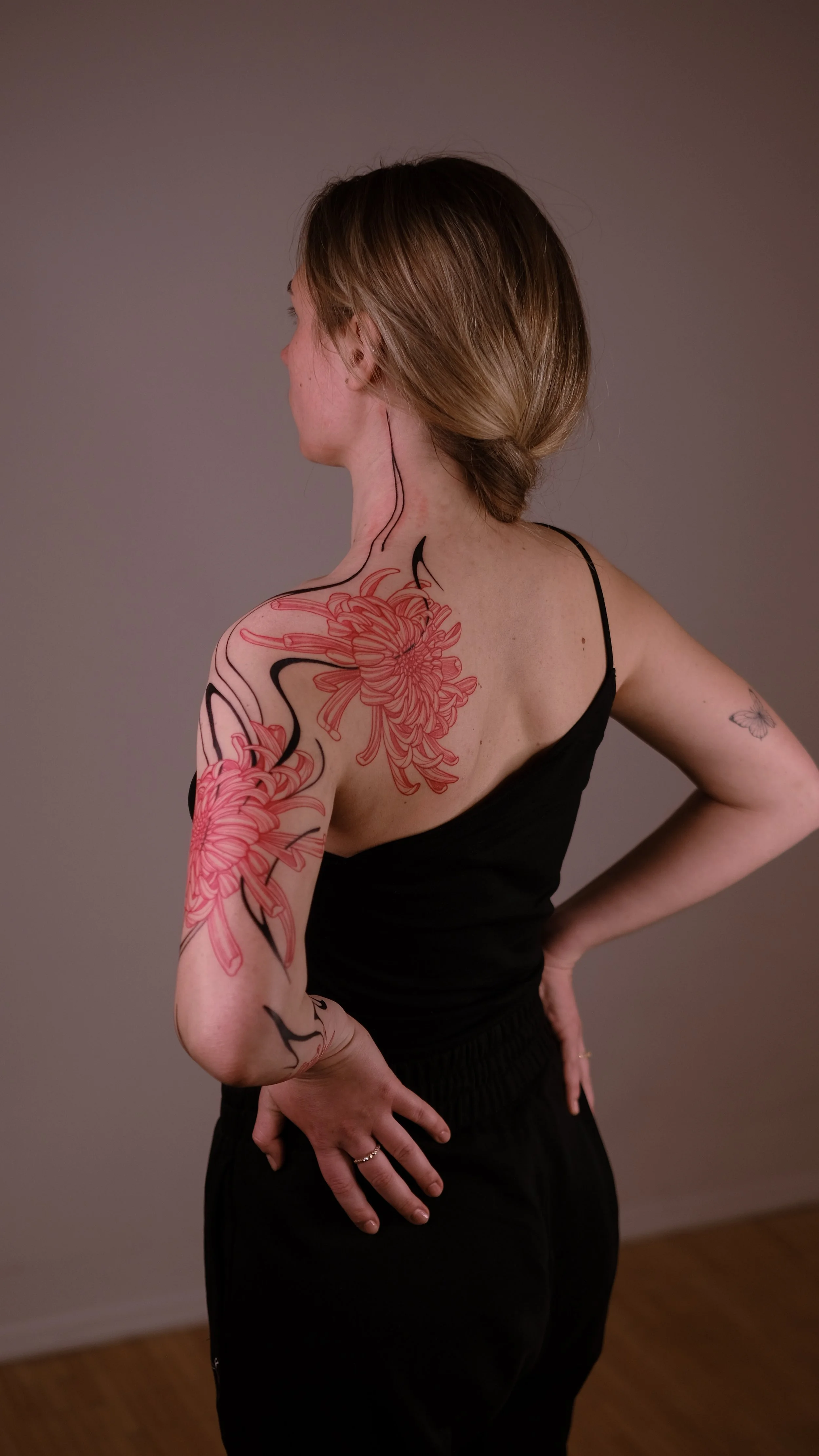 Woman with floral tattoos on back and arm, wearing black outfit, brown hair tied back.