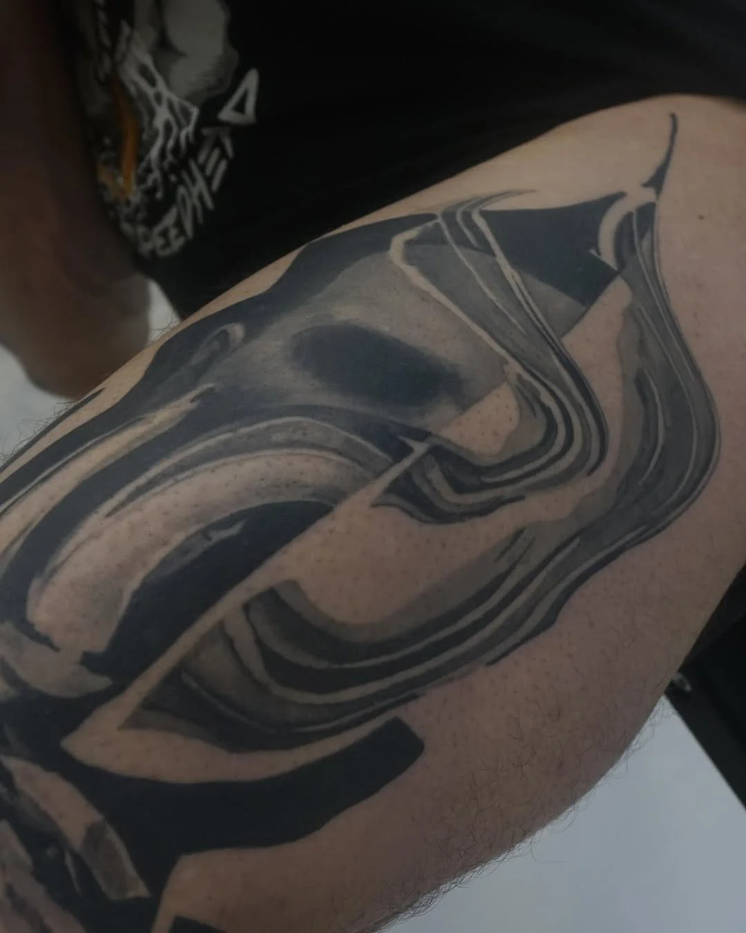 Close-up of a black abstract tattoo on a person's arm with swirling lines and shapes.