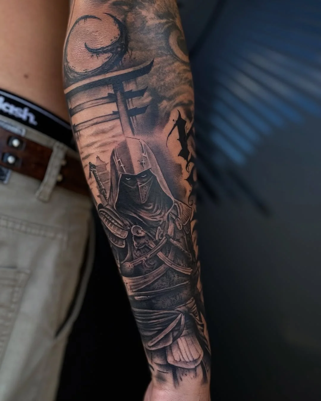 Black and gray tattoo of a warrior with armor and a helmet, holding a sword. Seen on a person's arm.