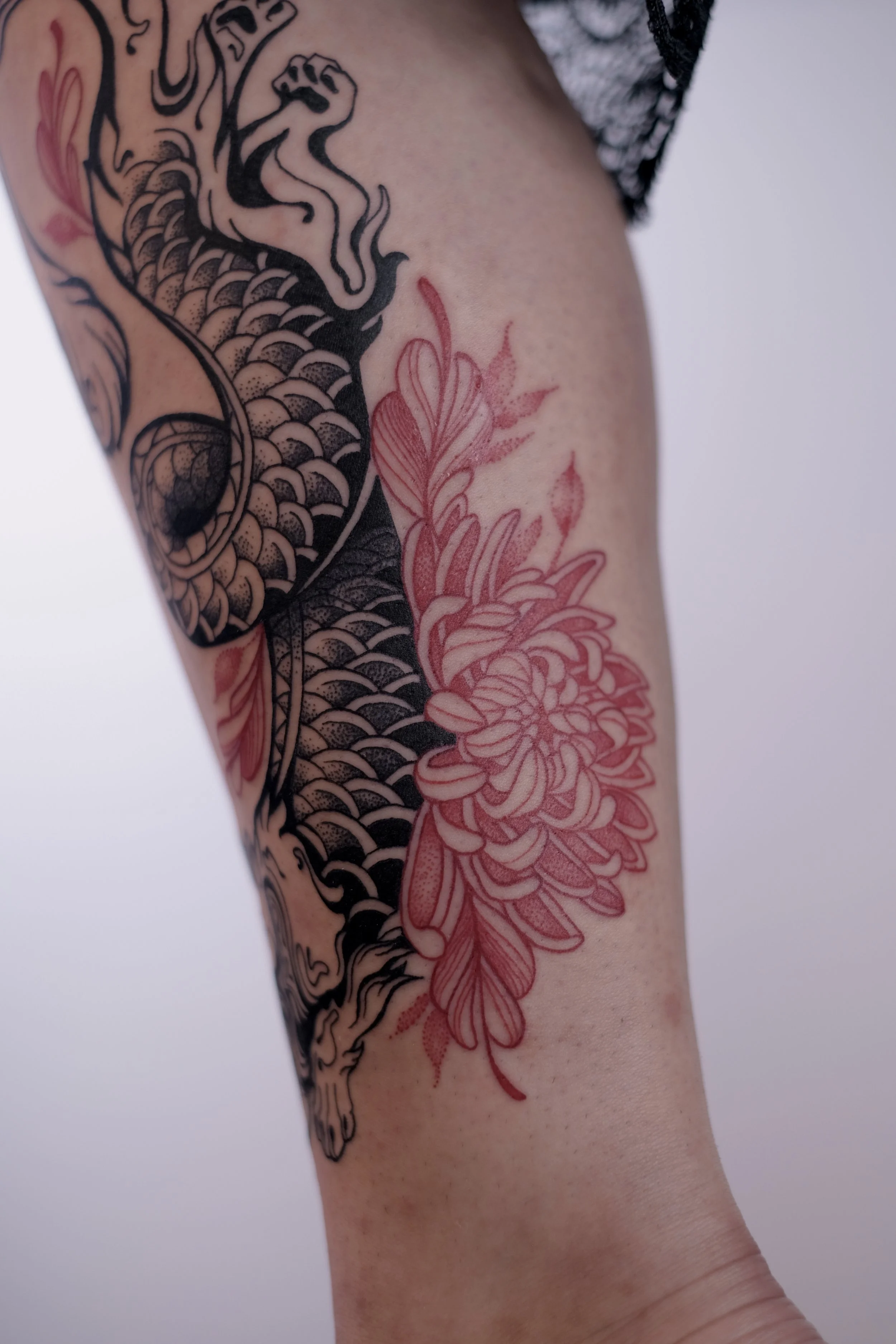 A tattoo featuring a black dragon with intricate scales and clawed paws, combined with a large pink floral design on a person's arm.