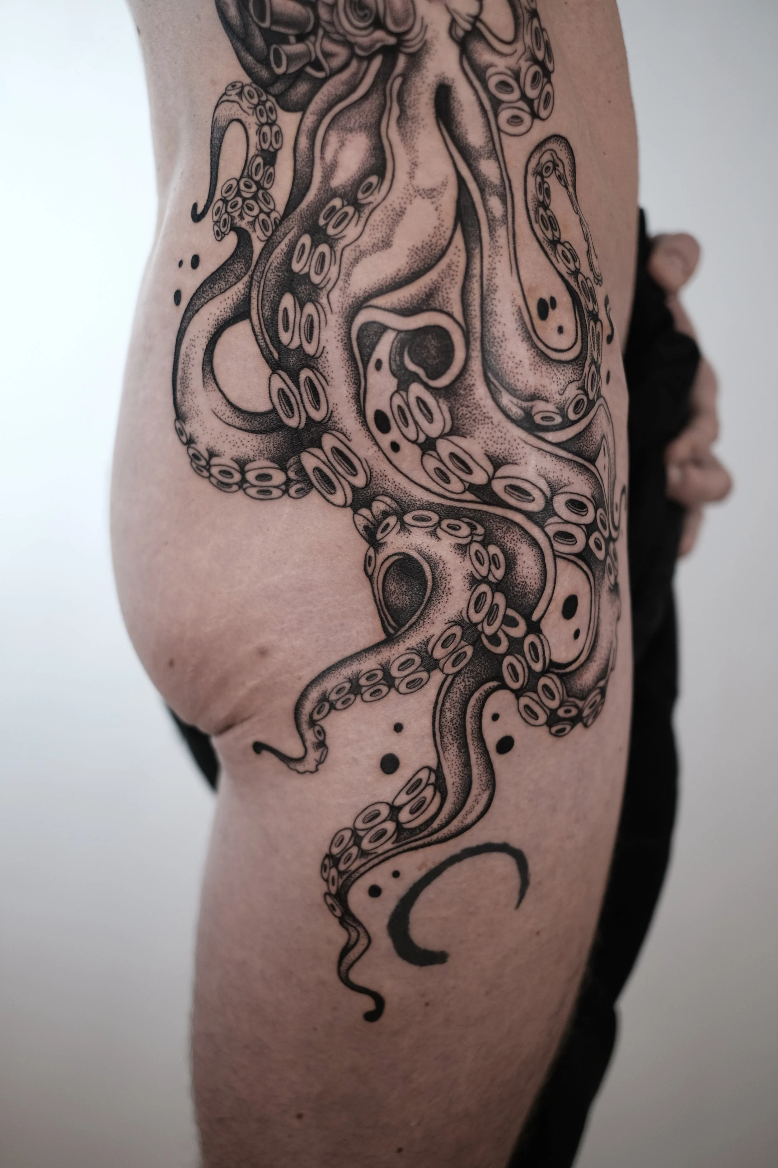 Tattoo of an octopus on a person's upper thigh. The octopus is depicted in black ink with detailed tentacles and suction cups.
