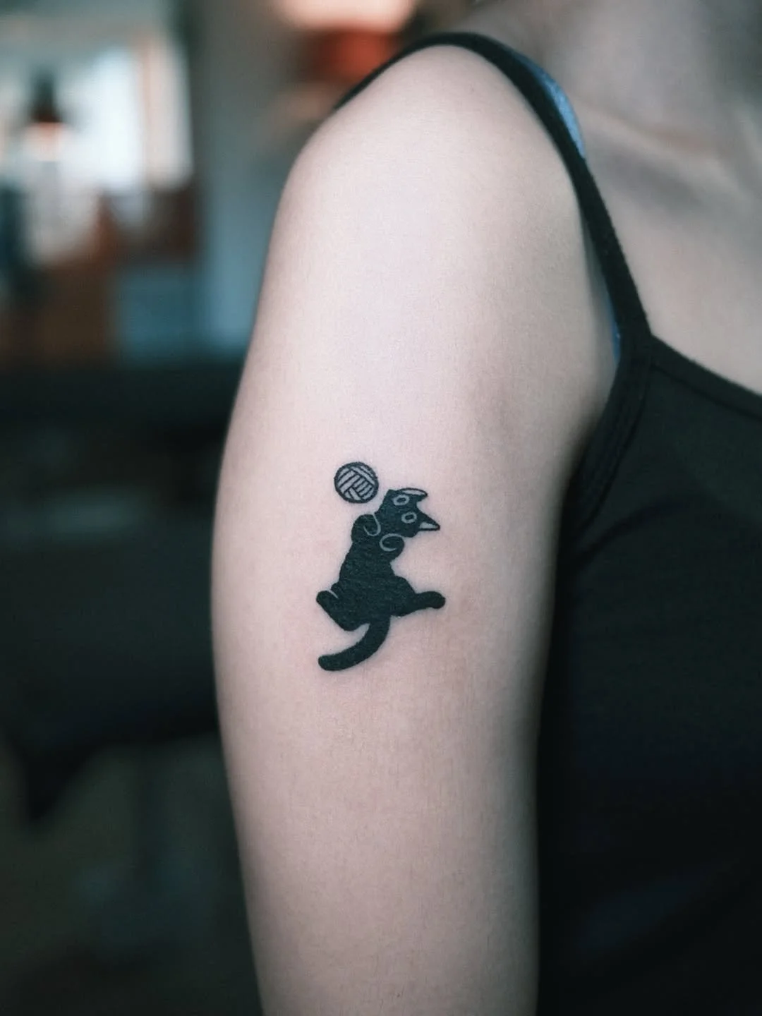 Tattoo of a black cartoon dog with a ball above its head on person's upper arm.