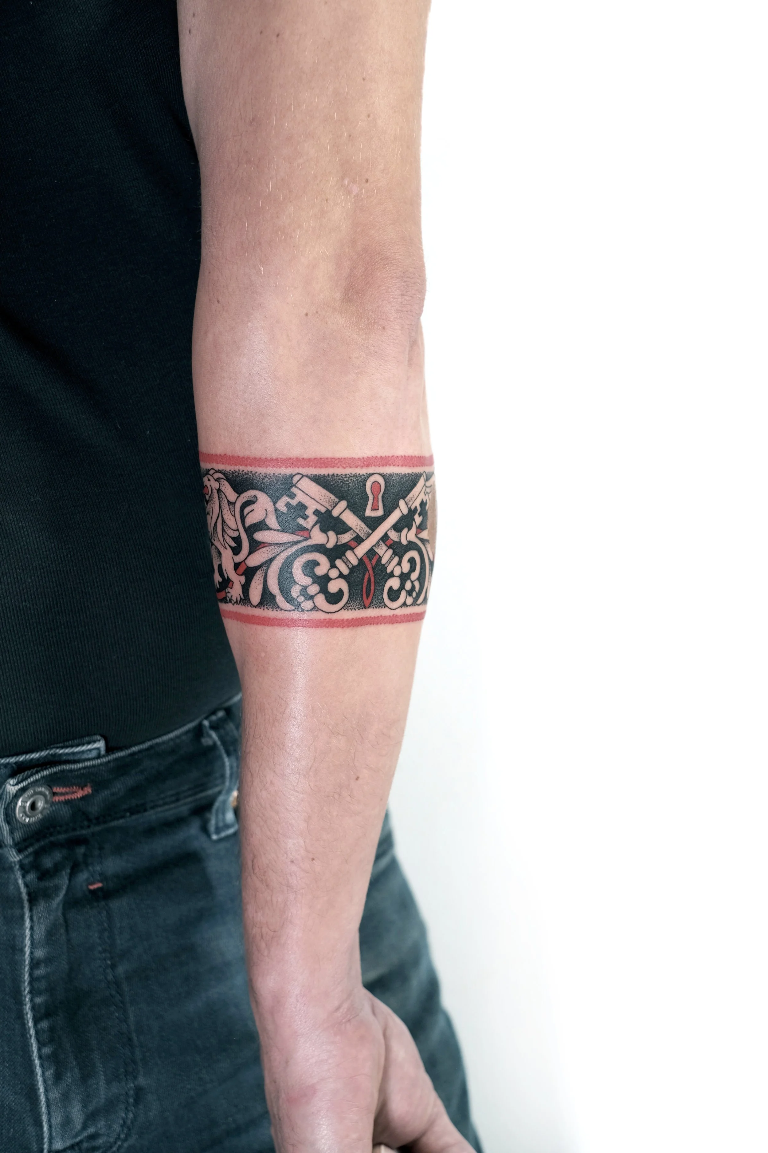 Tattoo of crossed swords, keys, and decorative patterns encased in a rectangular band around a person's arm.