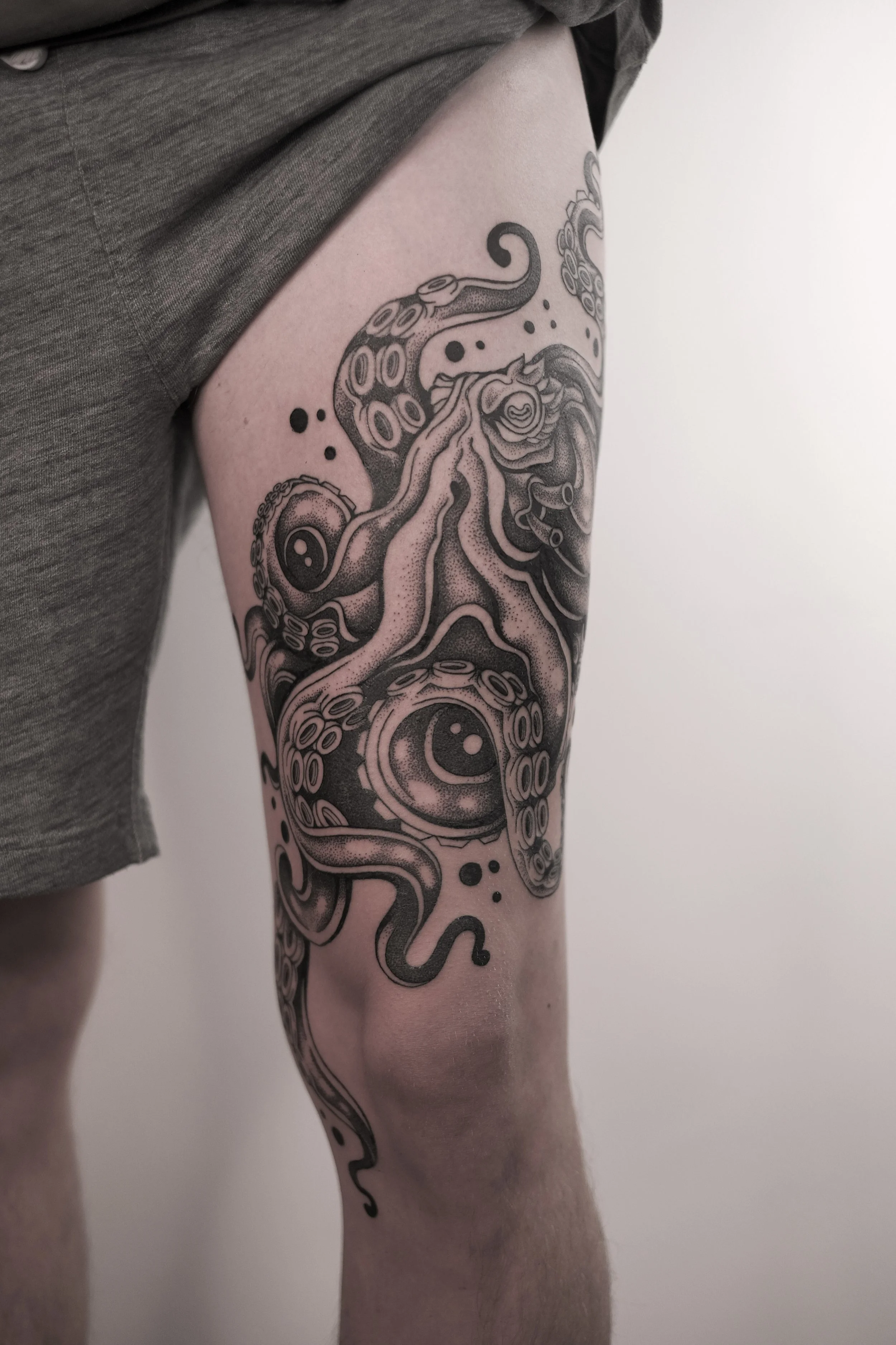 A black and gray tattoo of a stylized octopus with detailed tentacles and large eyes on a person's thigh.