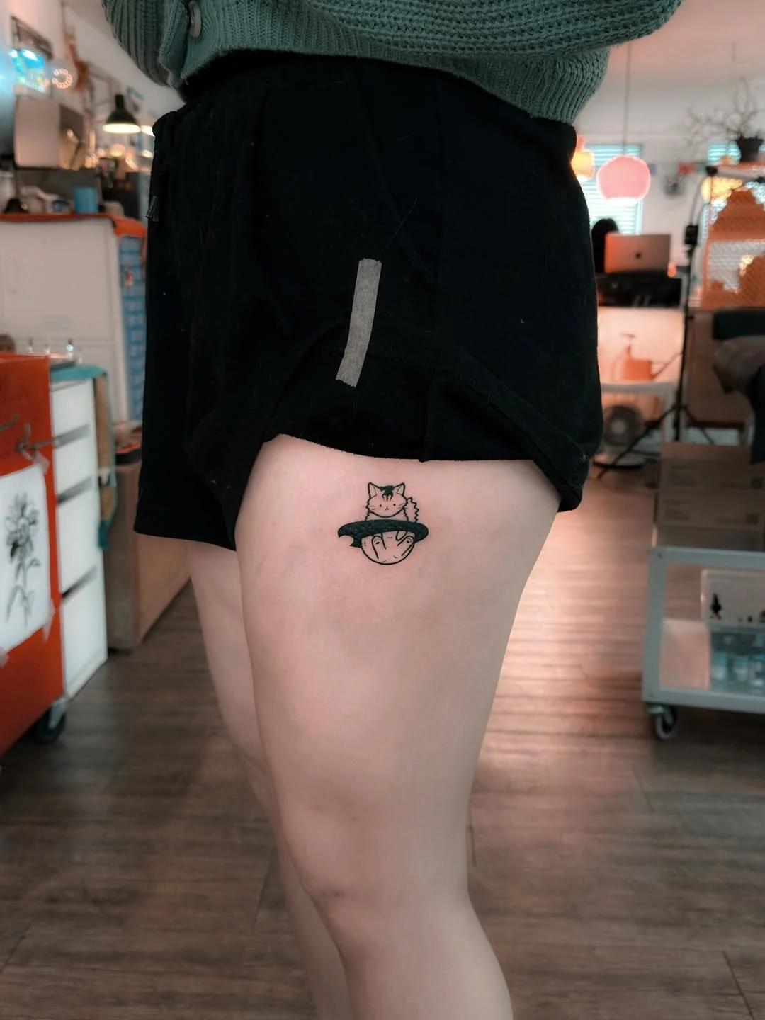 Tattoo of a cartoon-style cat in a bowl of ramen on person's upper thigh.