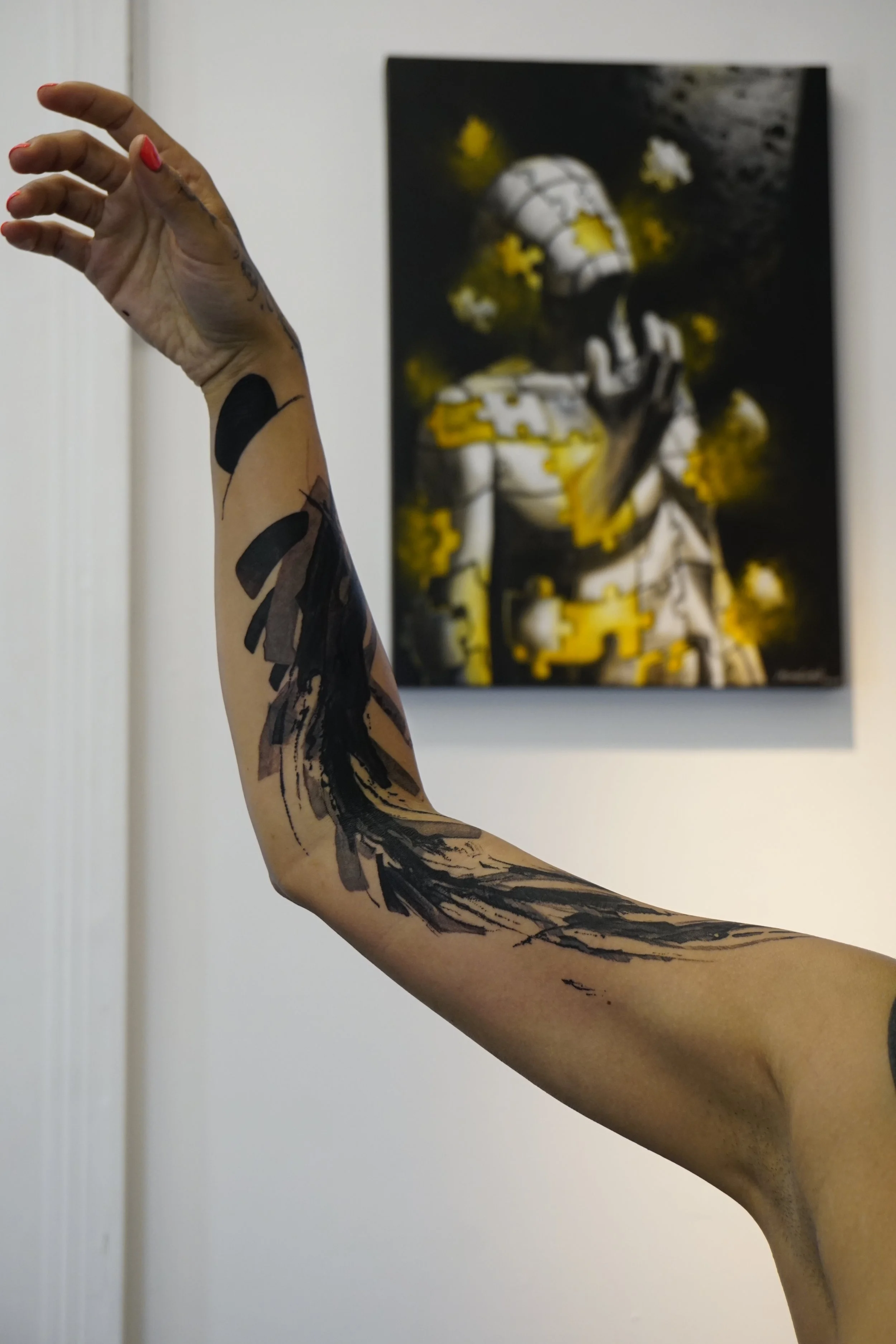 Tattooed arm raised in front of abstract art on wall
