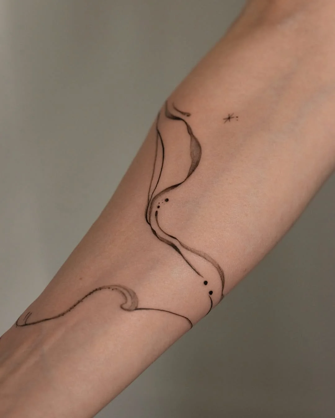 Minimalist black ink tattoo of a wavy line with small dots and a star on a person's forearm.