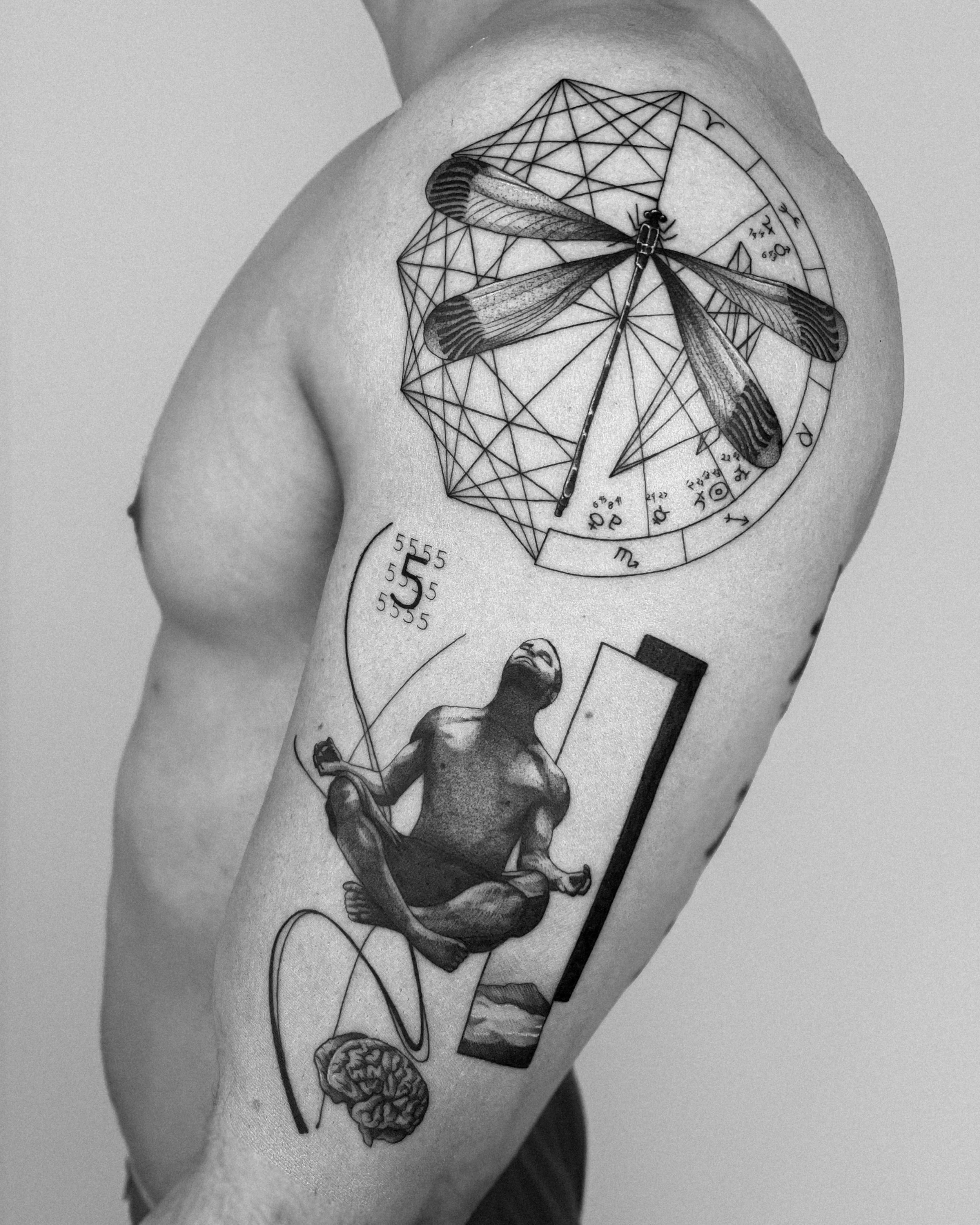 Tattoo on a person's upper arm featuring a dragonfly, geometric design, meditating figure, numerical sequences, and a brain.