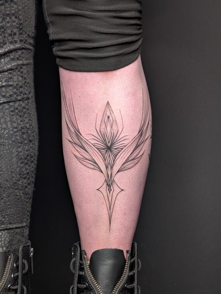 Black geometric tattoo on a person's calf featuring sharp lines and symmetrical shapes, resembling abstract wings or feathers.