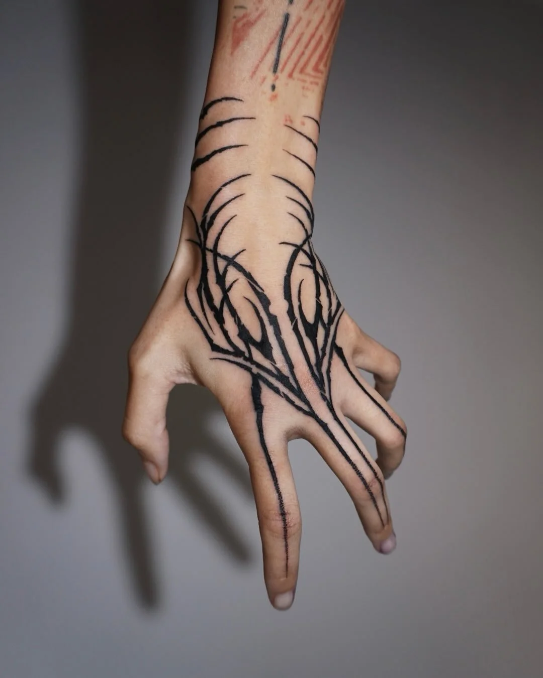 A hand with black ink tattoo outlines of abstract and tribal designs, running from the wrist to the fingers, with a red mark on the wrist.