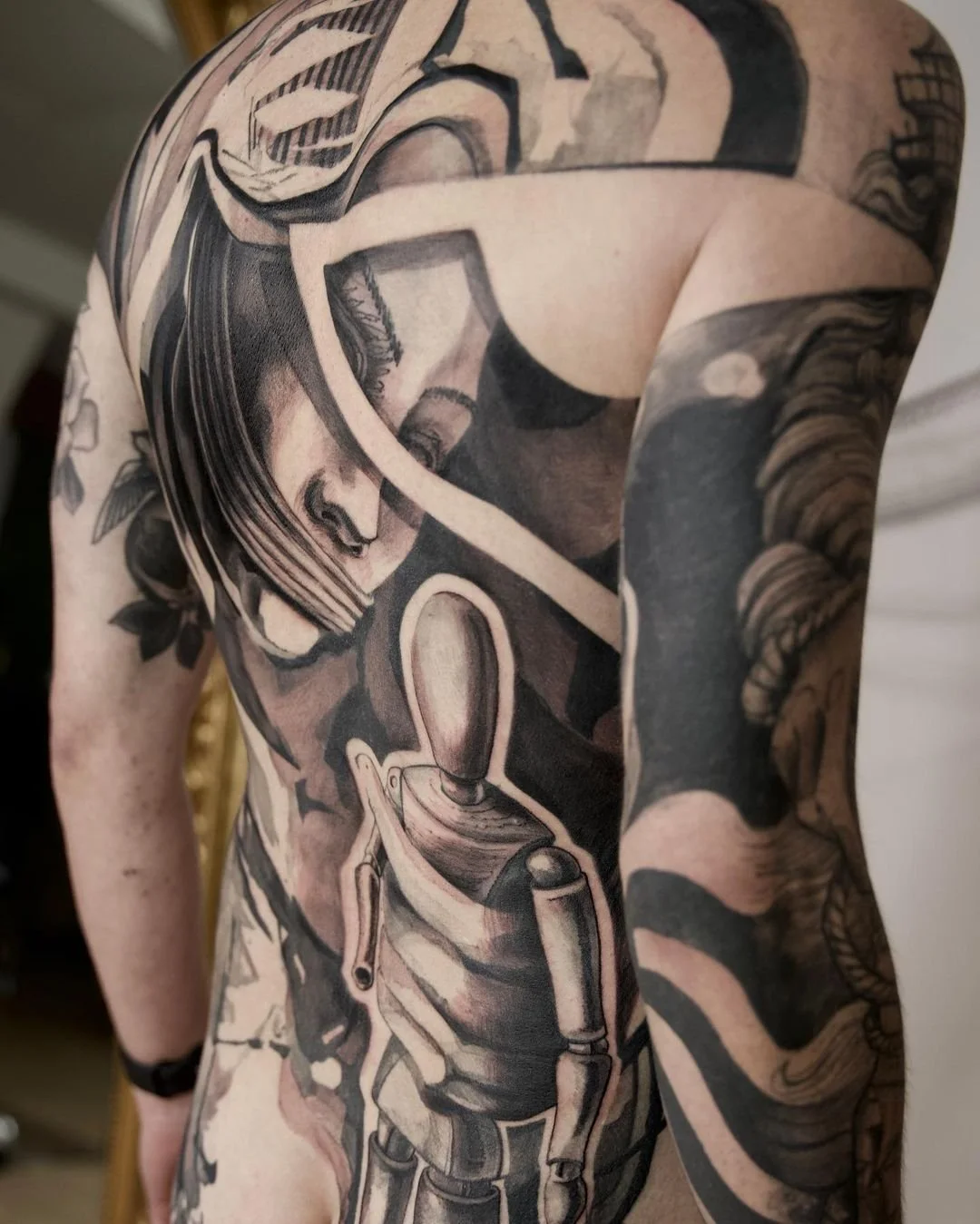Full back tattoo featuring abstract art with monochrome tones, including a stylized human face and an artist's mannequin.