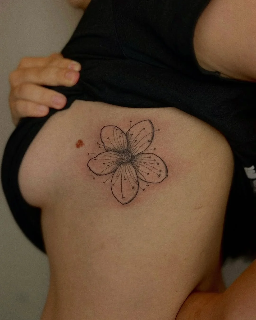 Tattoo of a detailed butterfly with delicate line work on person's upper arm, partially covered by a black shirt.