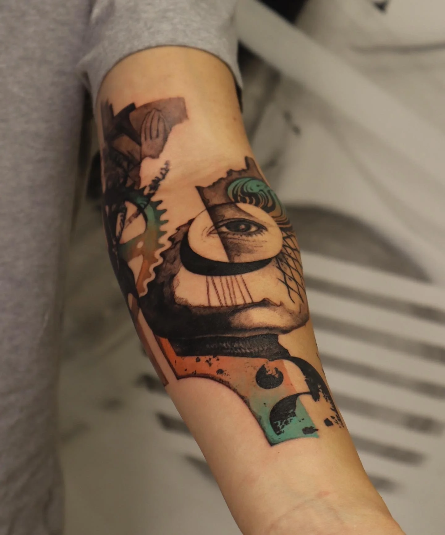 Abstract tattoo on forearm featuring a mix of geometric shapes, an eye, and various patterns.