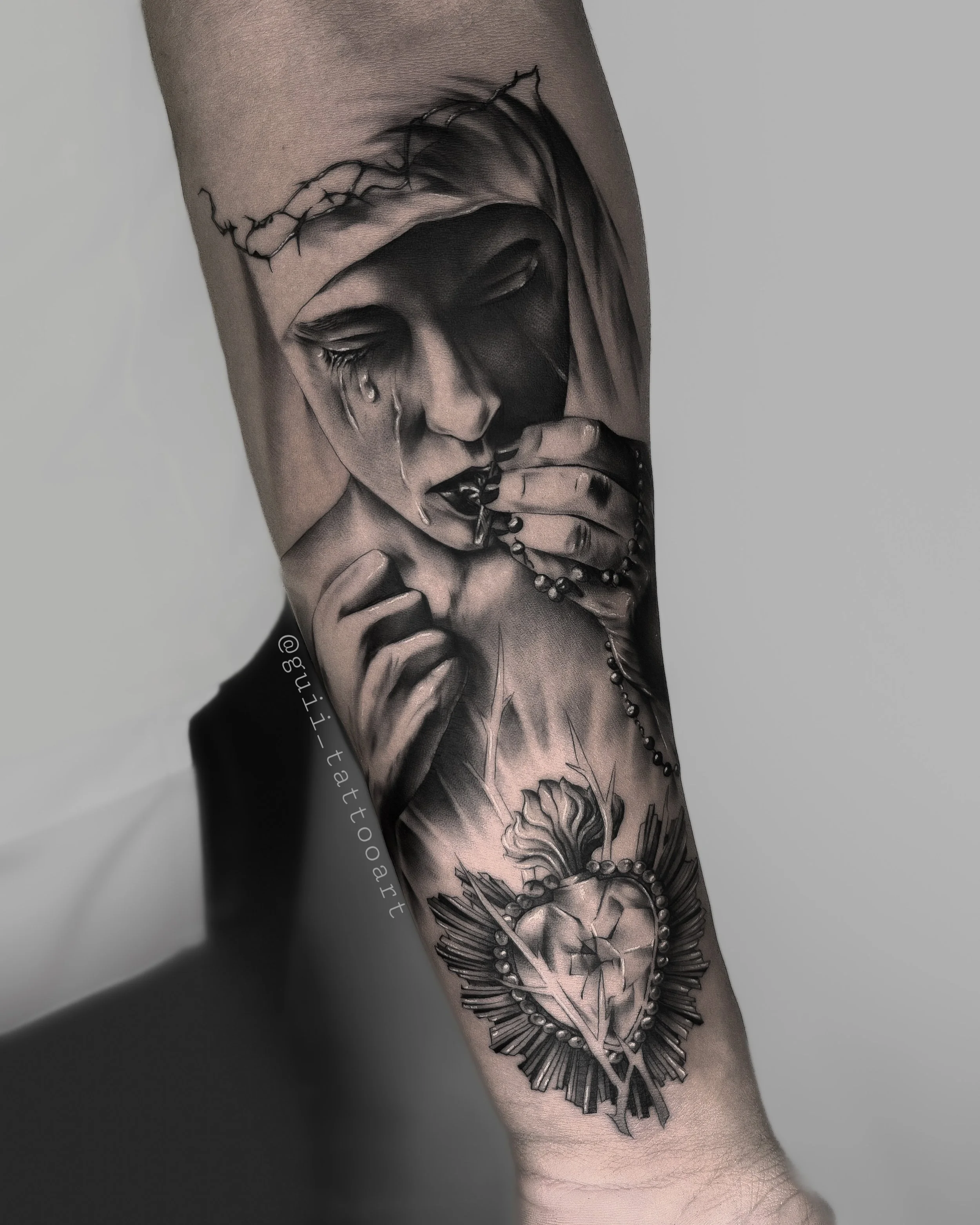 Black and gray tattoo of a tearful figure with a crown of thorns, holding rosary beads, and a Sacred Heart design.