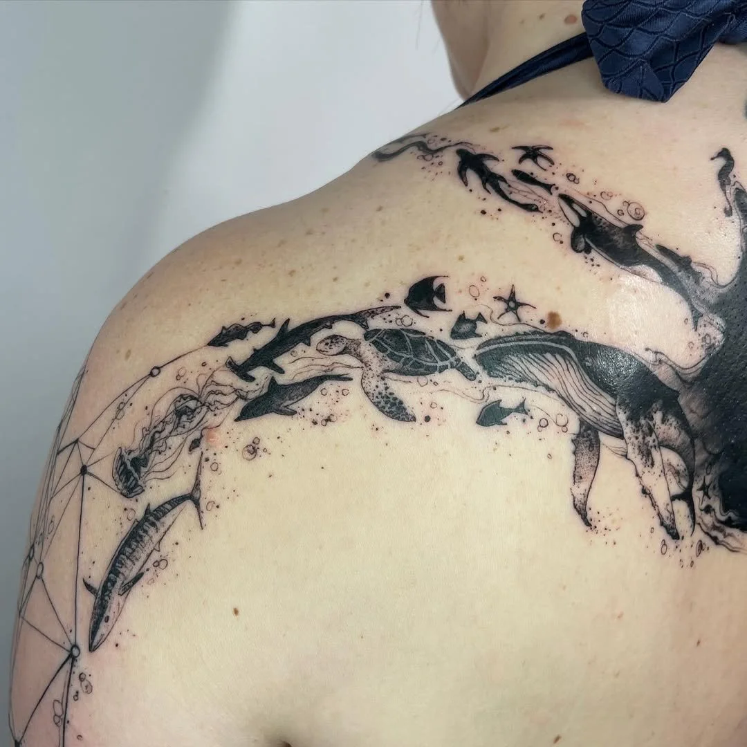 Tattoo of marine life on shoulder, featuring a whale, sea turtle, and various fish, including a shark.