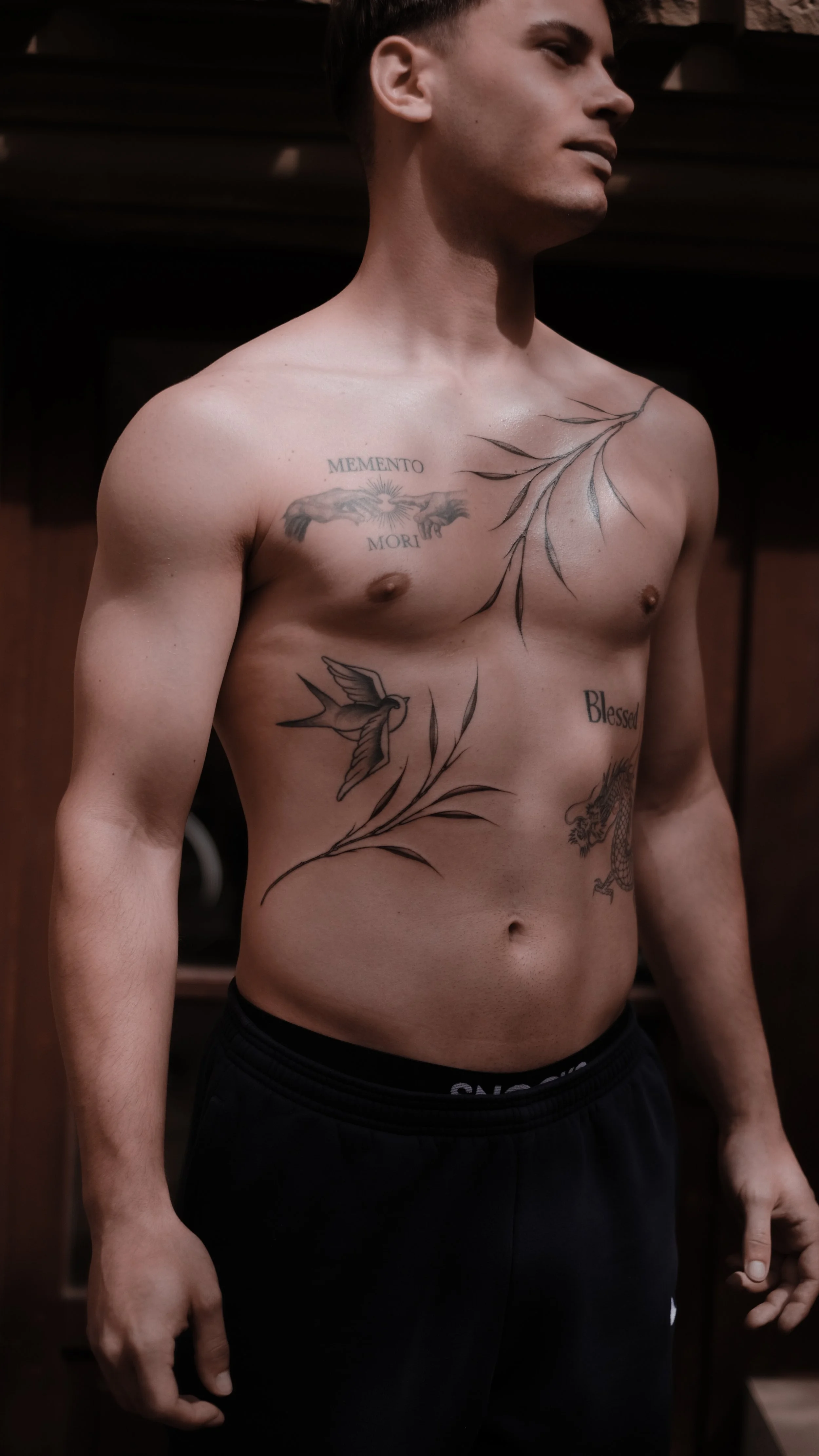 Shirtless man with various tattoos on chest and torso, wearing black pants.