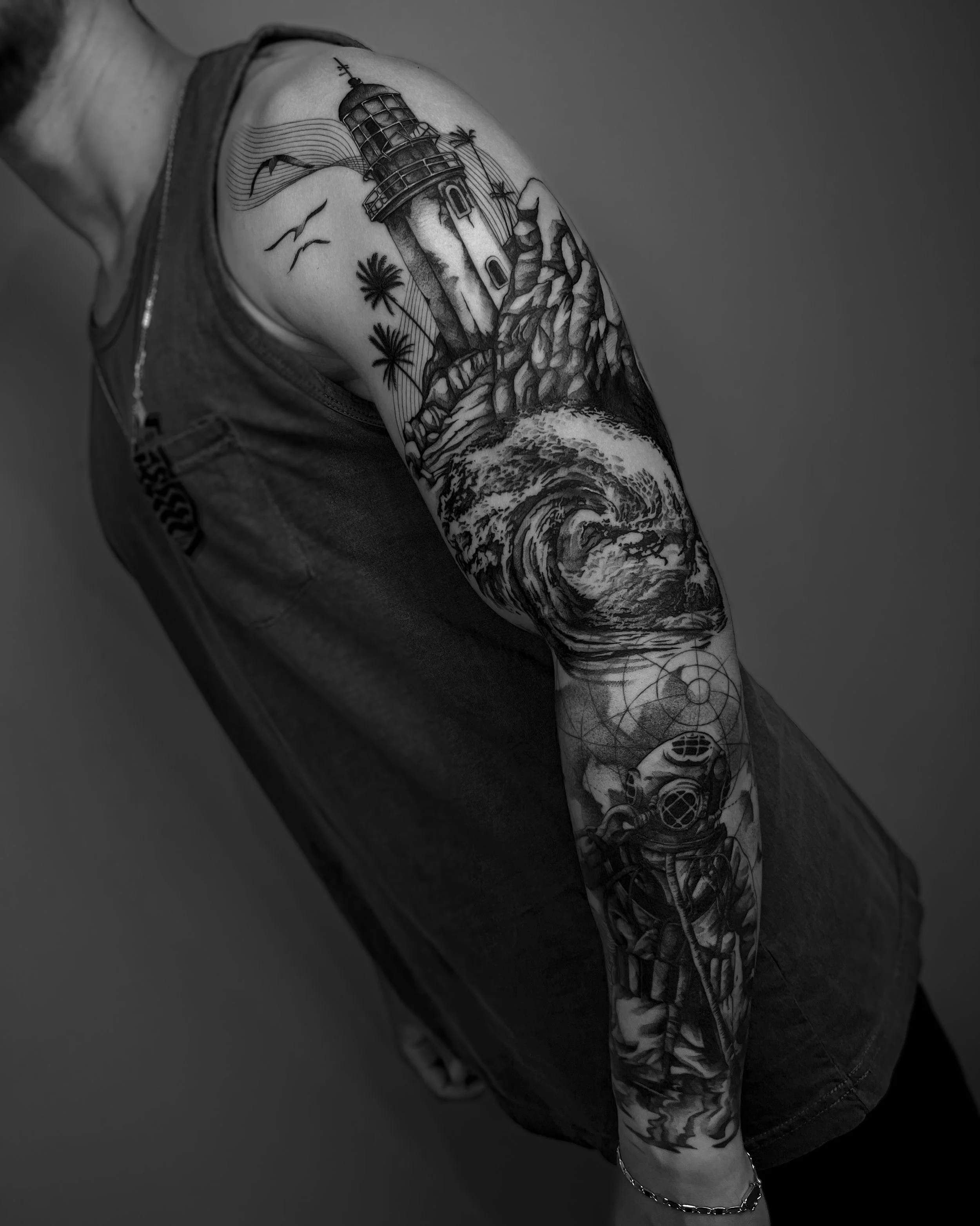 Arm tattoo featuring a lighthouse, ocean waves, palm trees, and a vintage diving helmet.