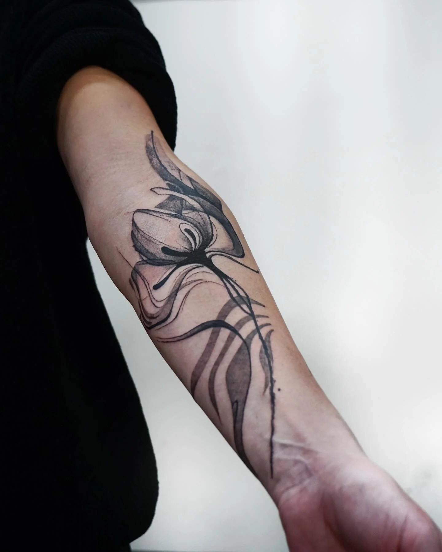 Black ink abstract butterfly tattoo on a person's upper arm.