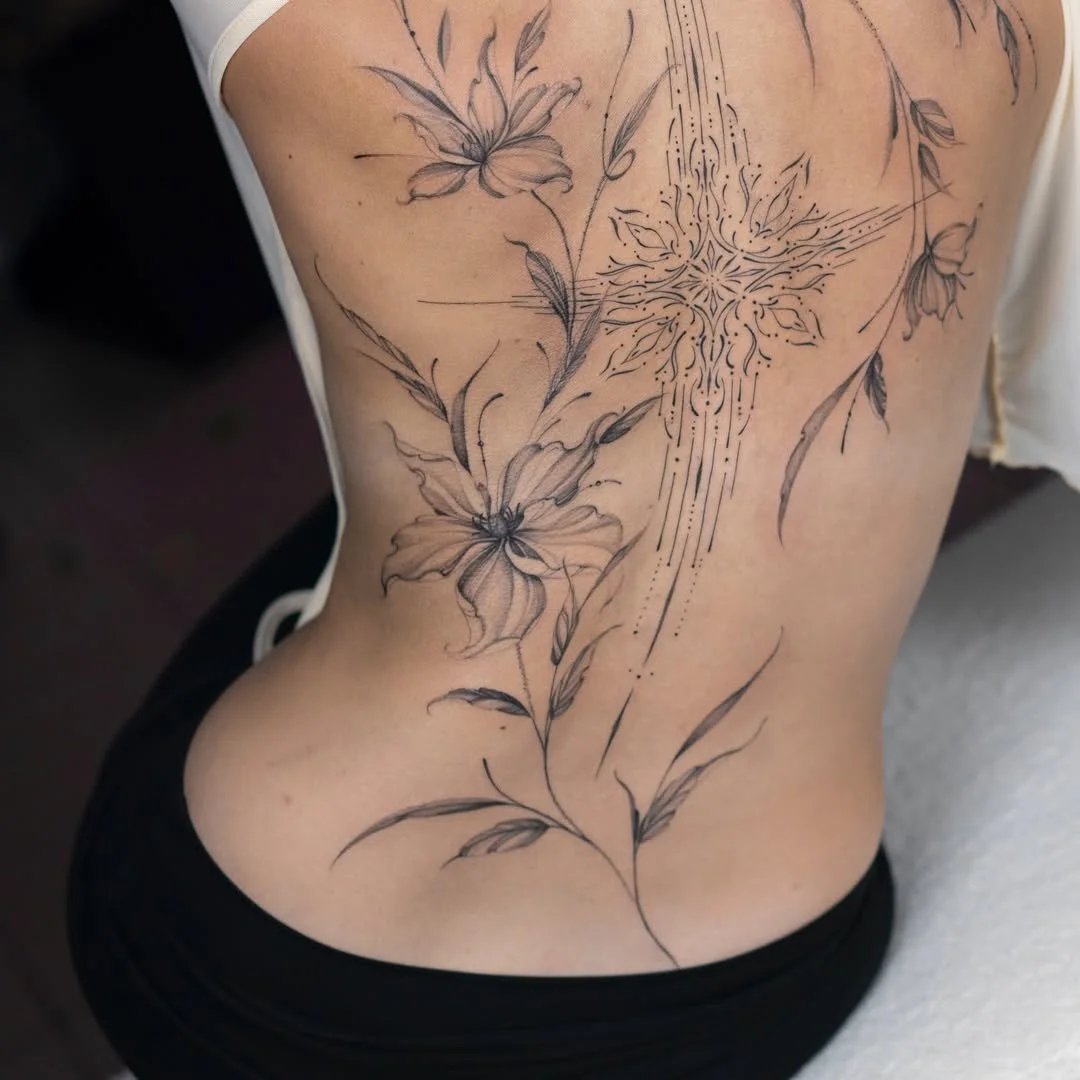 A person's side torso with a black ink floral tattoo, including lilies and a star-shaped geometric pattern, on the skin.