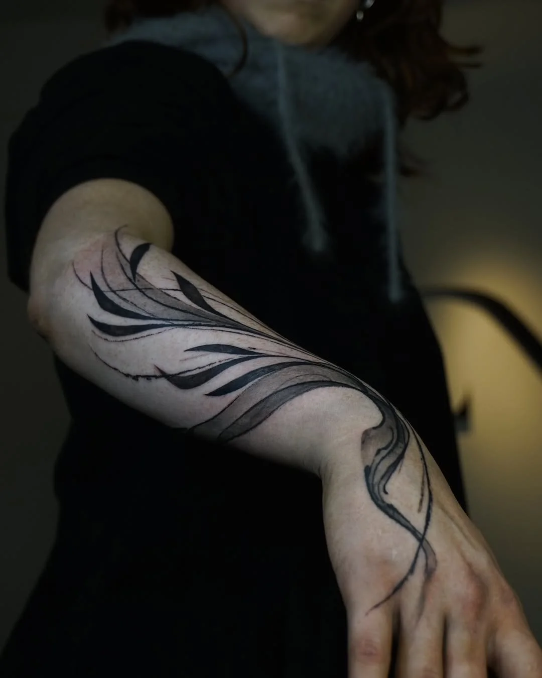 Person with an abstract black tattoo of stylized leaves on their forearm.