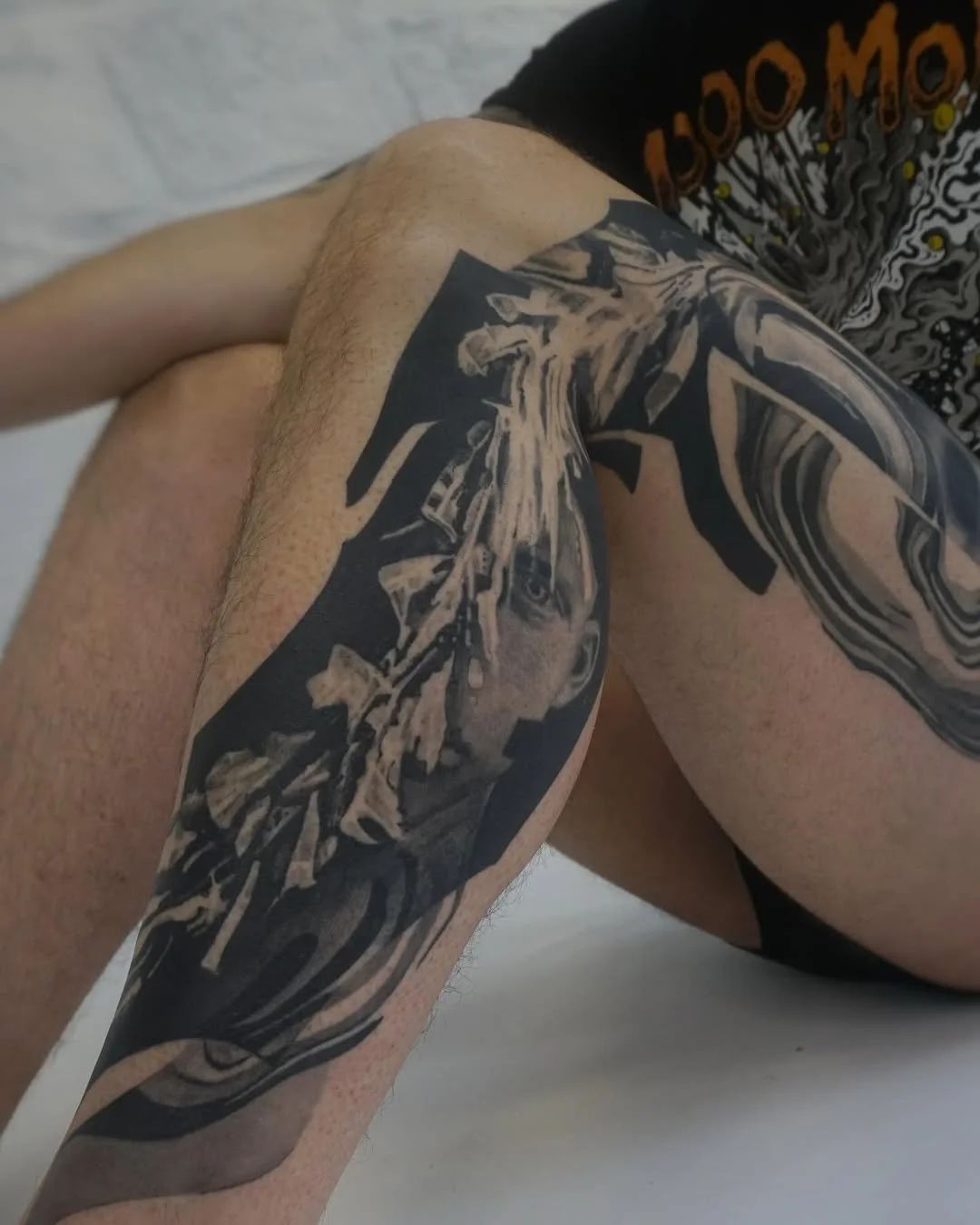 Close-up of a person's arm with a detailed black and gray tattoo of a face, likely a woman, and abstract swirling designs.