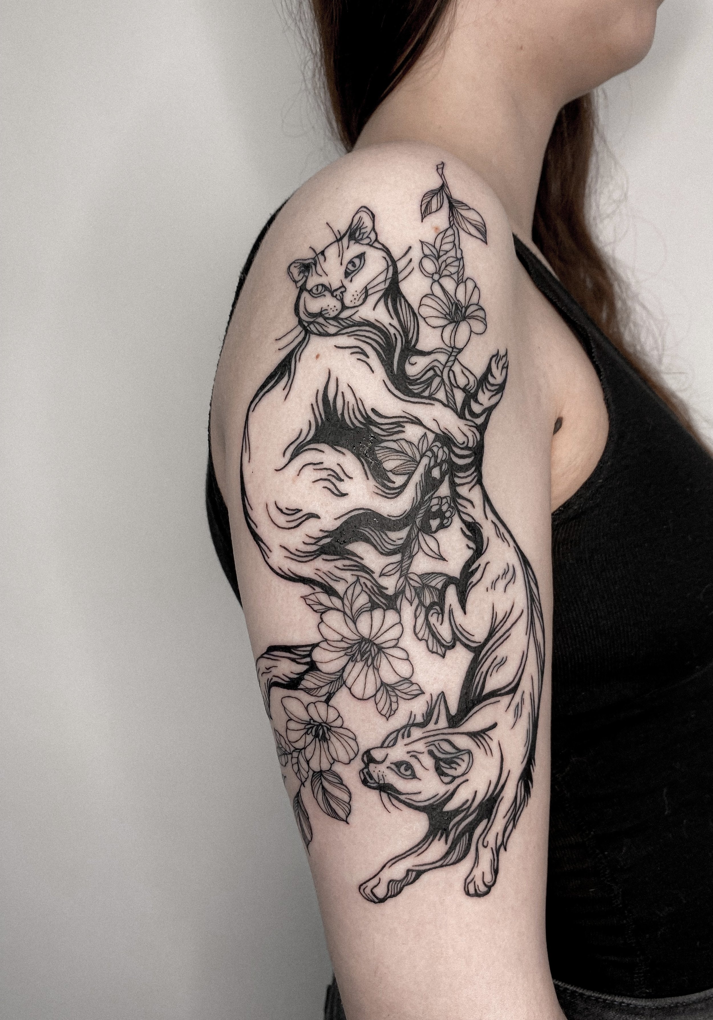Tattoo of a lion and tiger intertwined with flowers on a woman's upper arm.