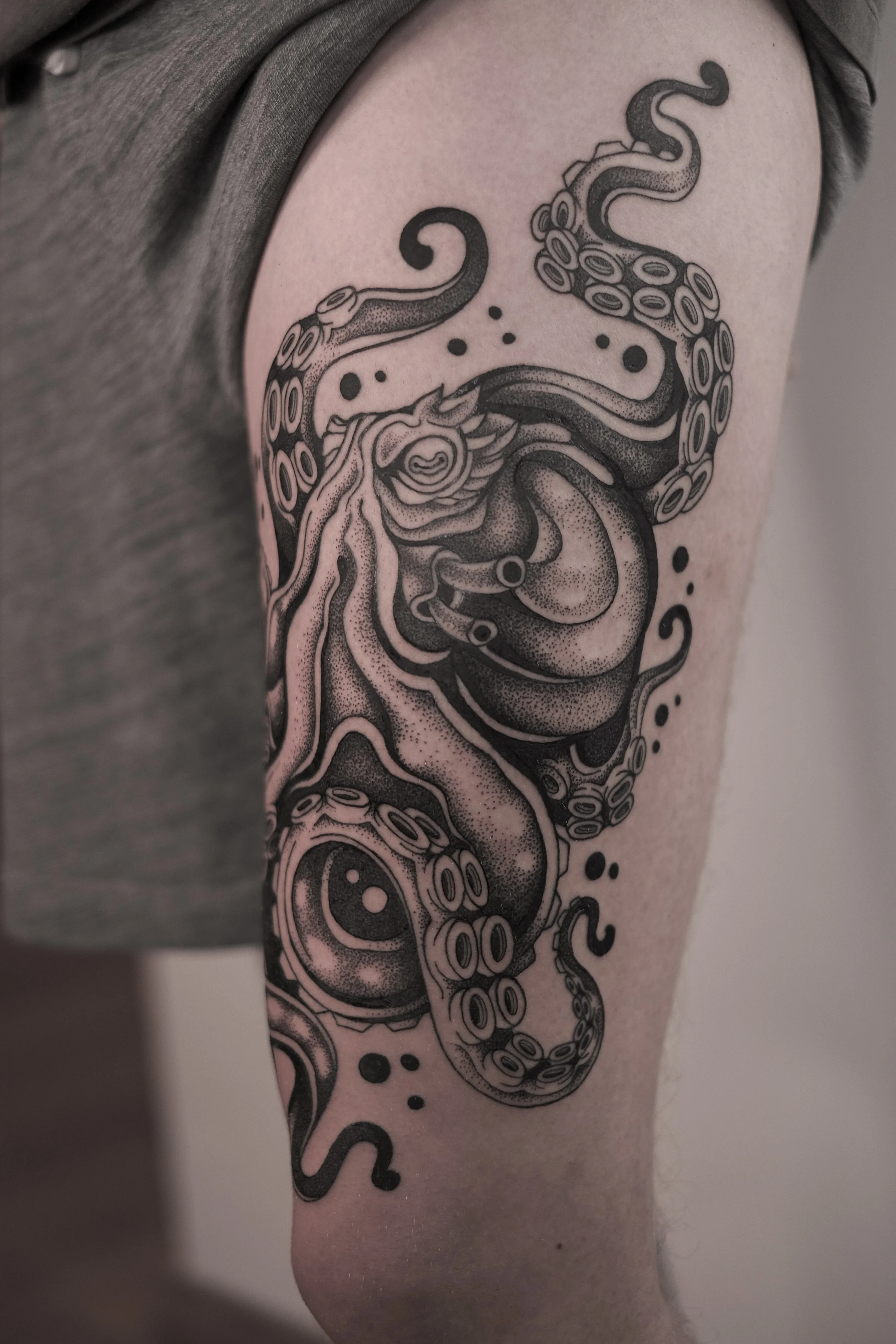 A black ink tattoo of an octopus located on a person's thigh.
