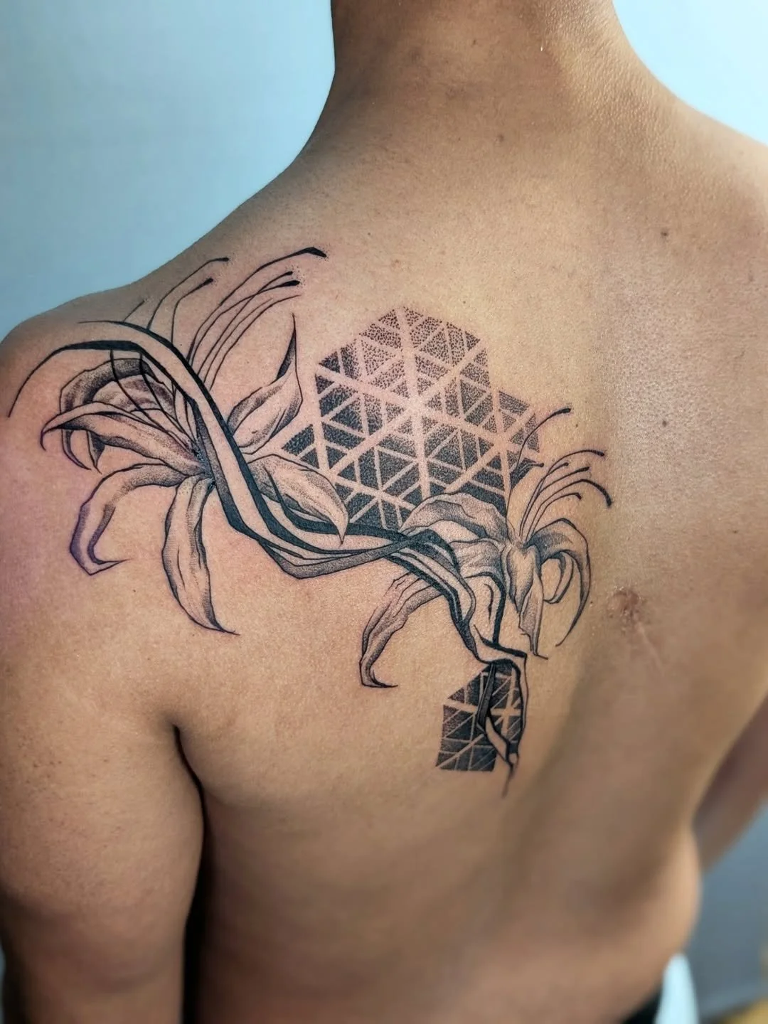 Tattoo of lilies and geometric patterns on a person's shoulder and upper chest.