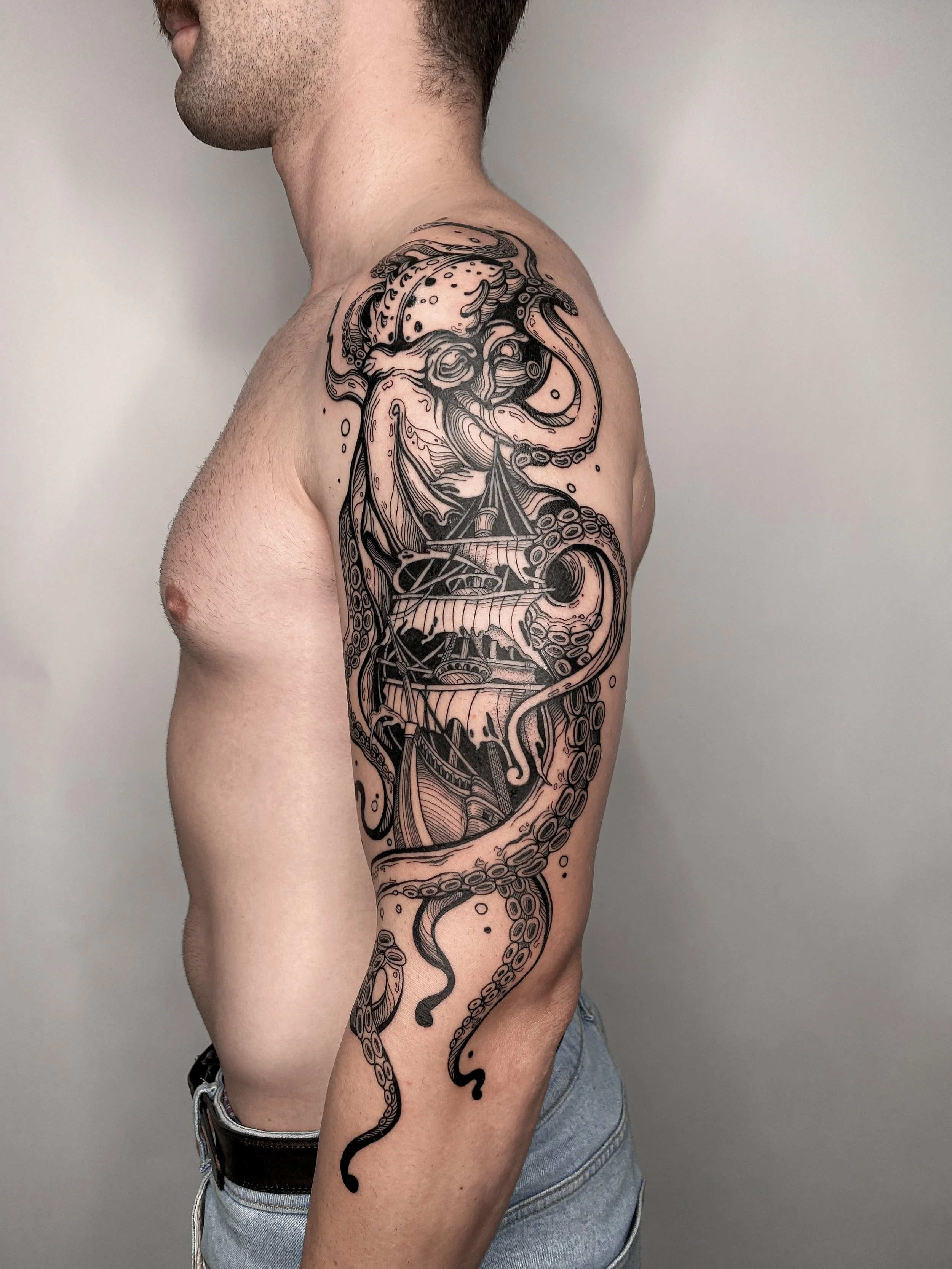 A man with a detailed black ink tattoo on his upper arm, shoulder, and part of his chest, depicting an intricate octopus intertwined with elements of a ship and waves.